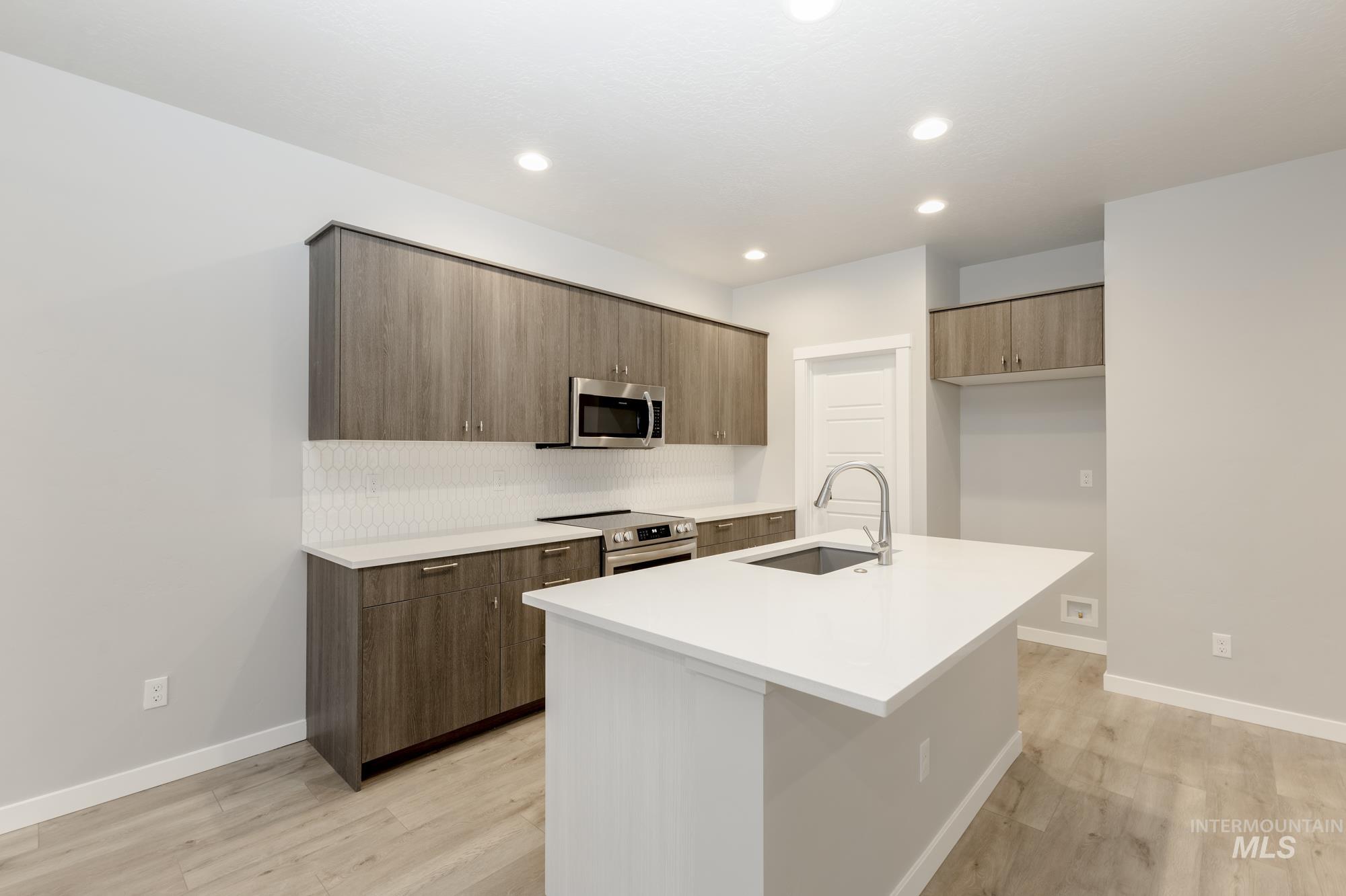 Kitchen with modern cabinets, stainless steel appliances, tasteful backsplash, light wood-style flooring, and an island with sink