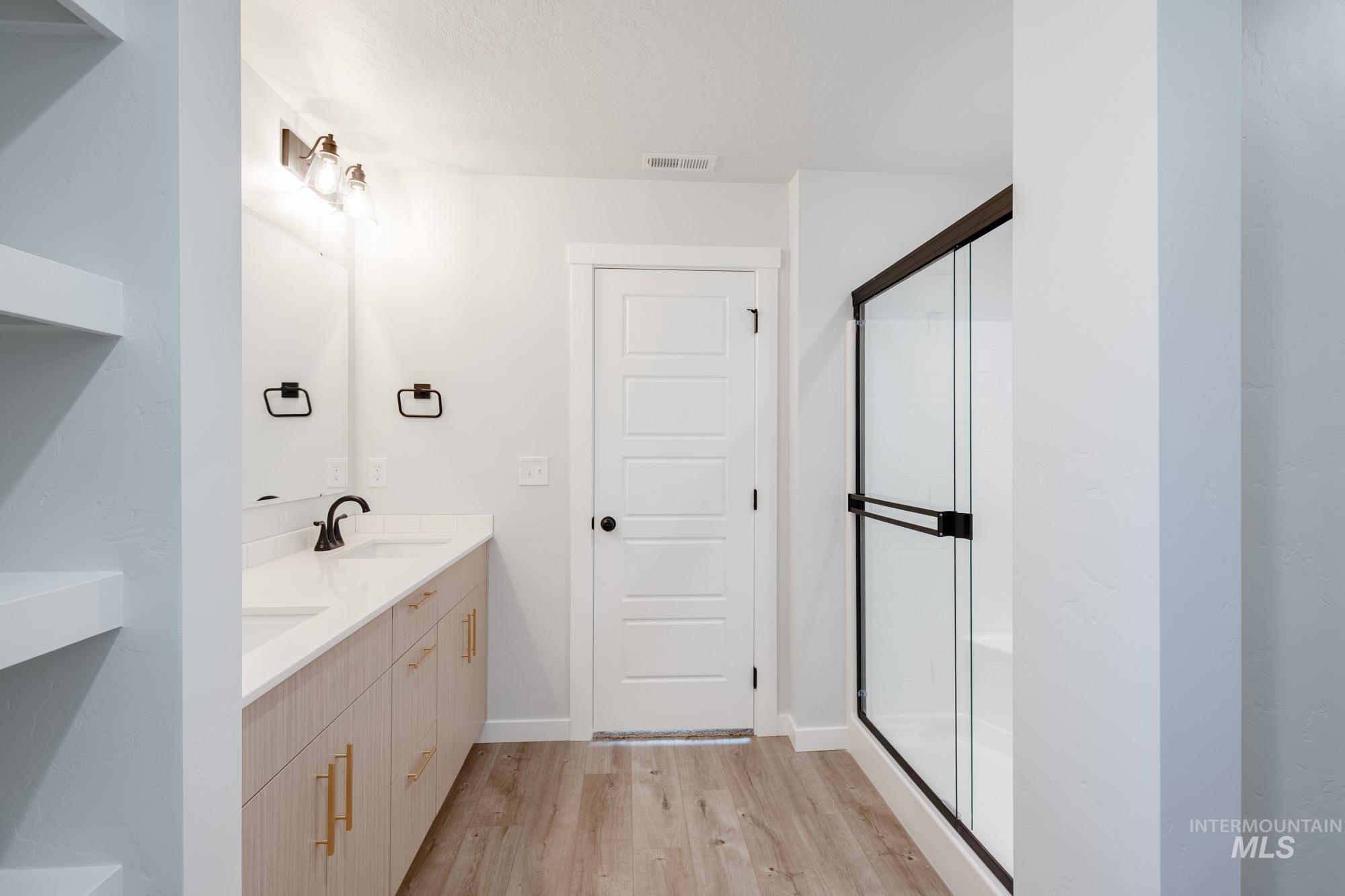 Bathroom with double vanity, a shower stall, and light wood-style floors