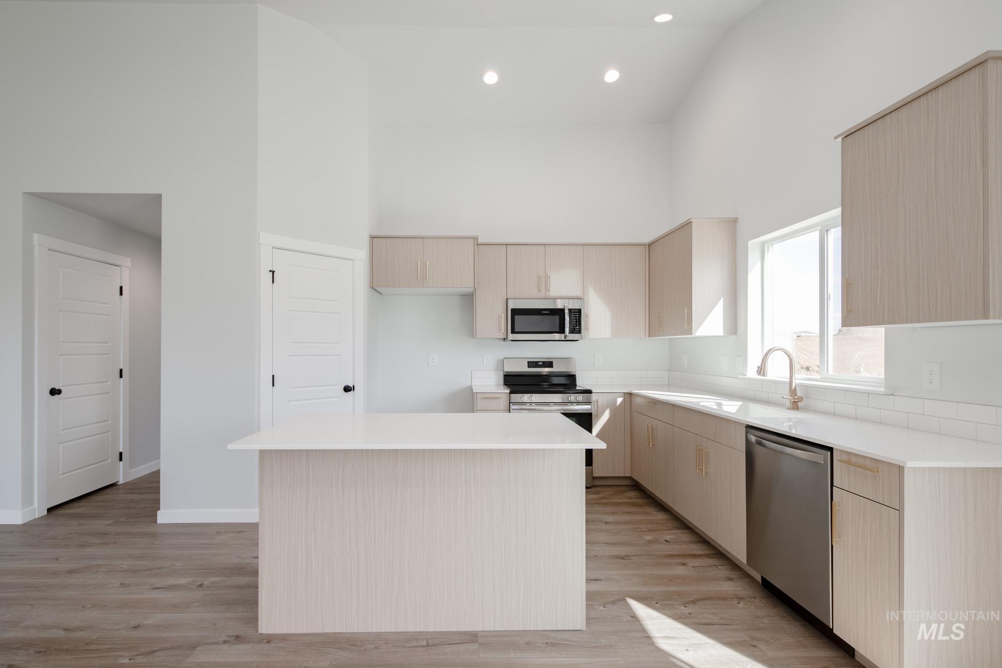 Kitchen featuring light brown cabinetry, a center island, high vaulted ceiling, appliances with stainless steel finishes, and light wood-style flooring