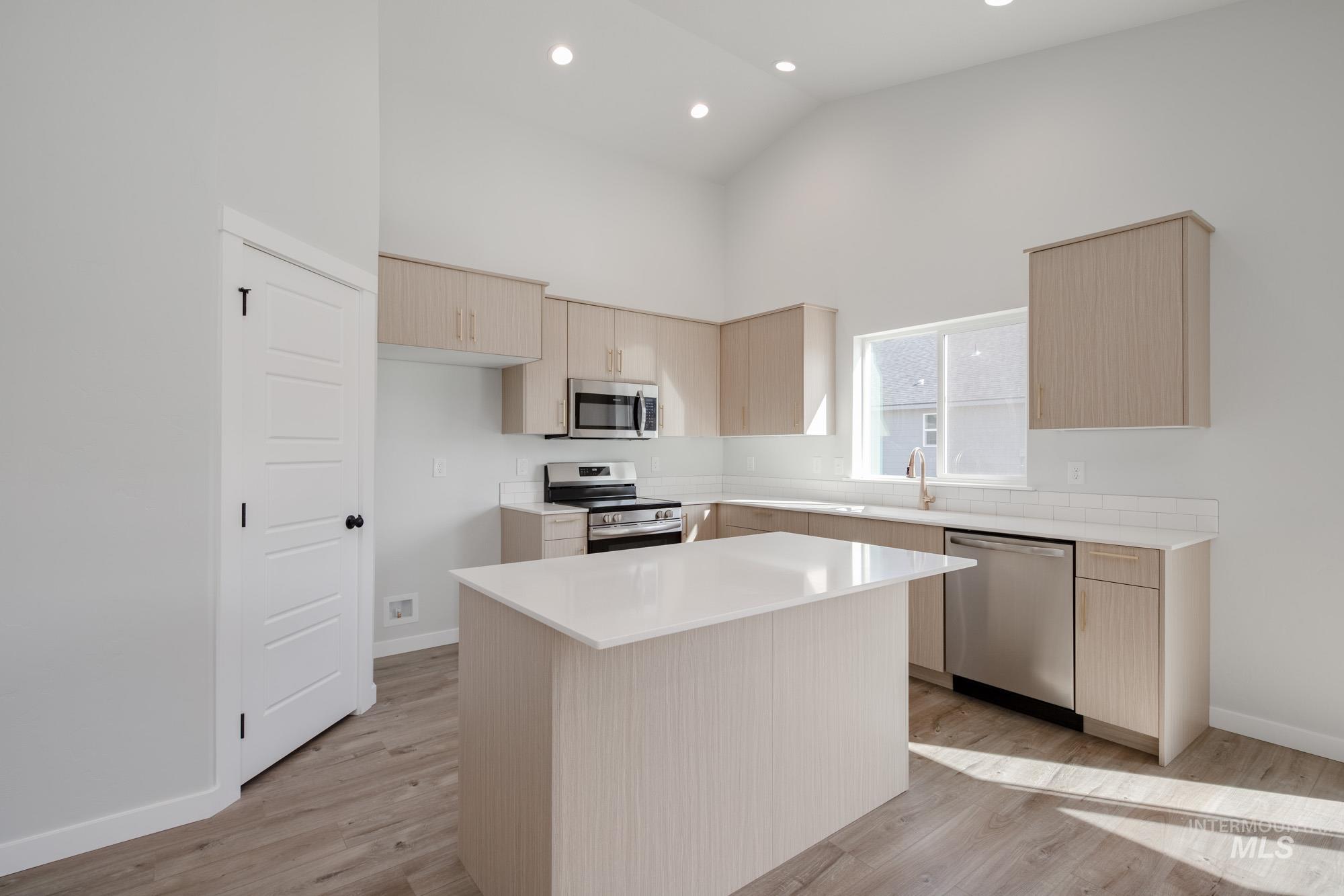 Kitchen featuring light brown cabinets, stainless steel appliances, a center island, light wood finished floors, and high vaulted ceiling