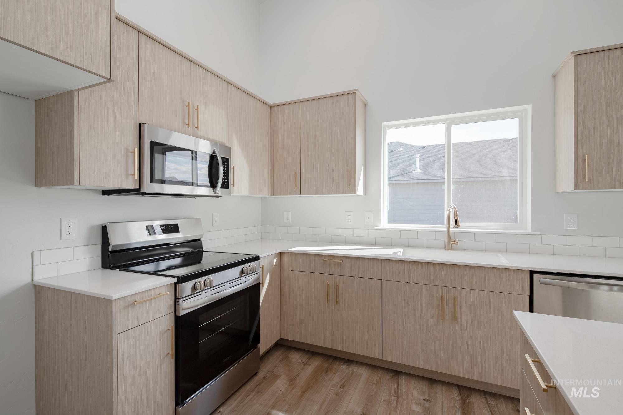 Kitchen with light brown cabinets, stainless steel appliances, modern cabinets, light wood-type flooring, and light stone counters