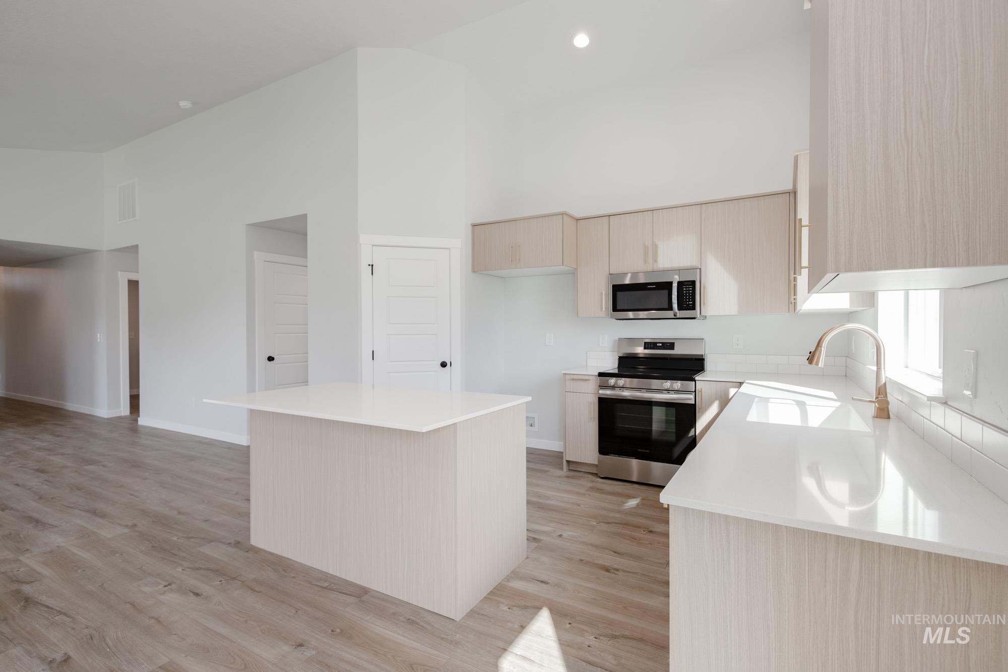 Kitchen with appliances with stainless steel finishes, a center island, a high ceiling, light brown cabinetry, and light wood-style floors