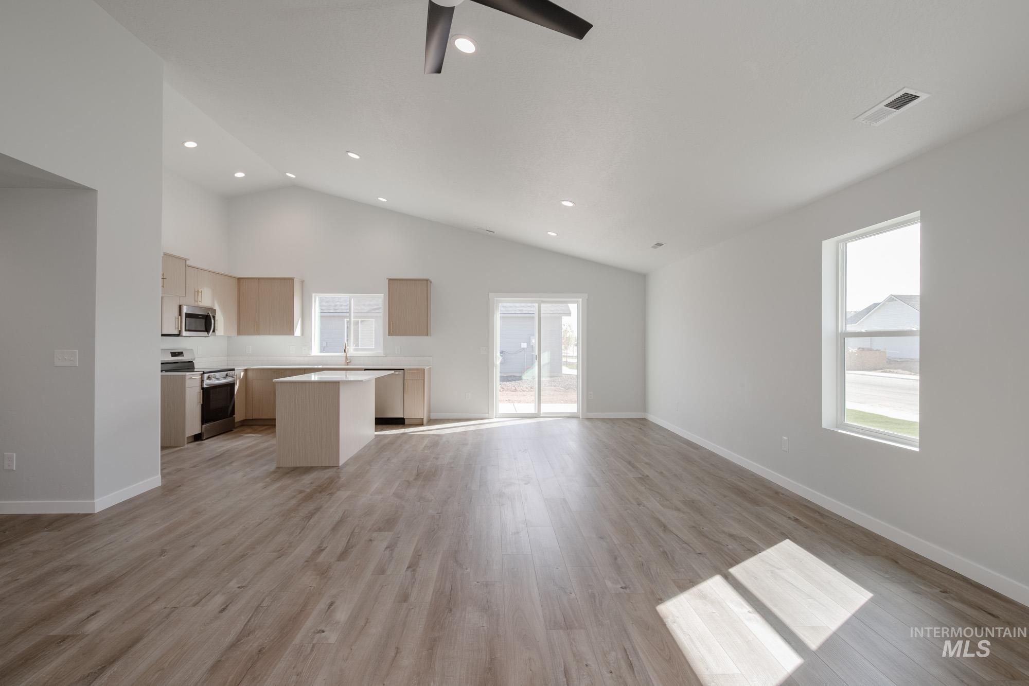Kitchen featuring open floor plan, a kitchen island, light countertops, stainless steel appliances, and light wood-type flooring