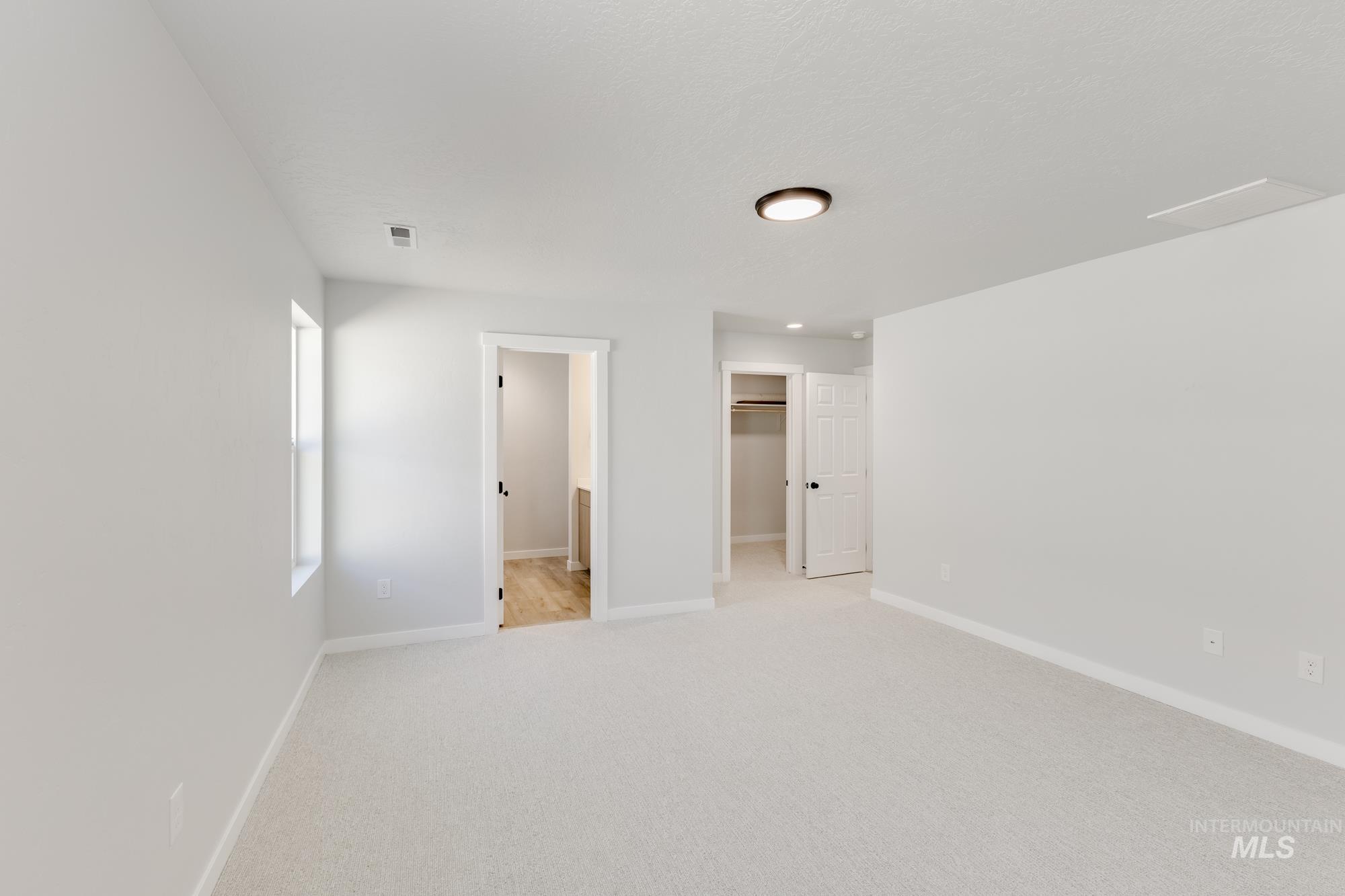 Unfurnished bedroom with ensuite bathroom, a spacious closet, and light colored carpet