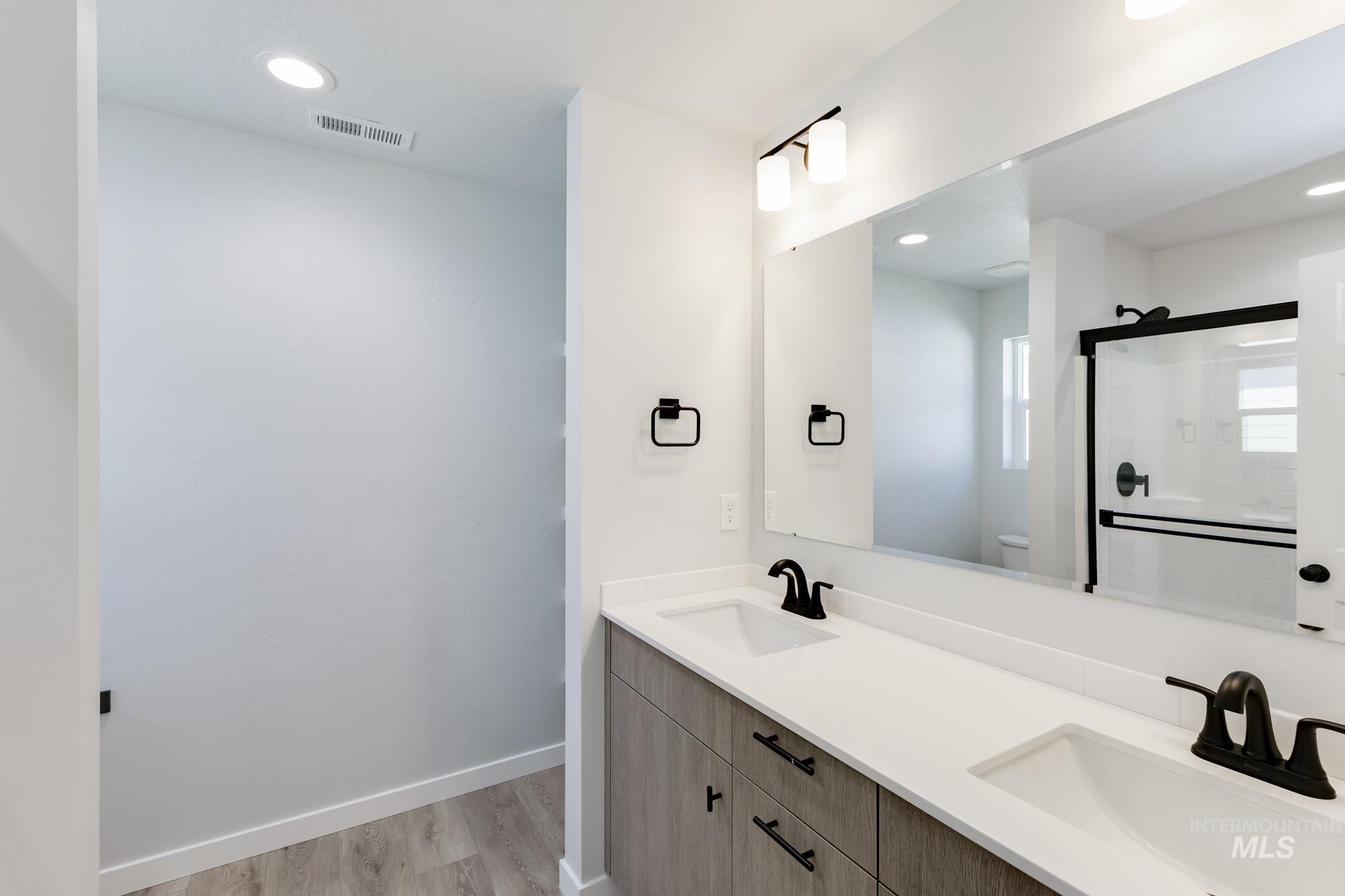 Full bath with double vanity, a shower stall, light wood-style floors, and recessed lighting
