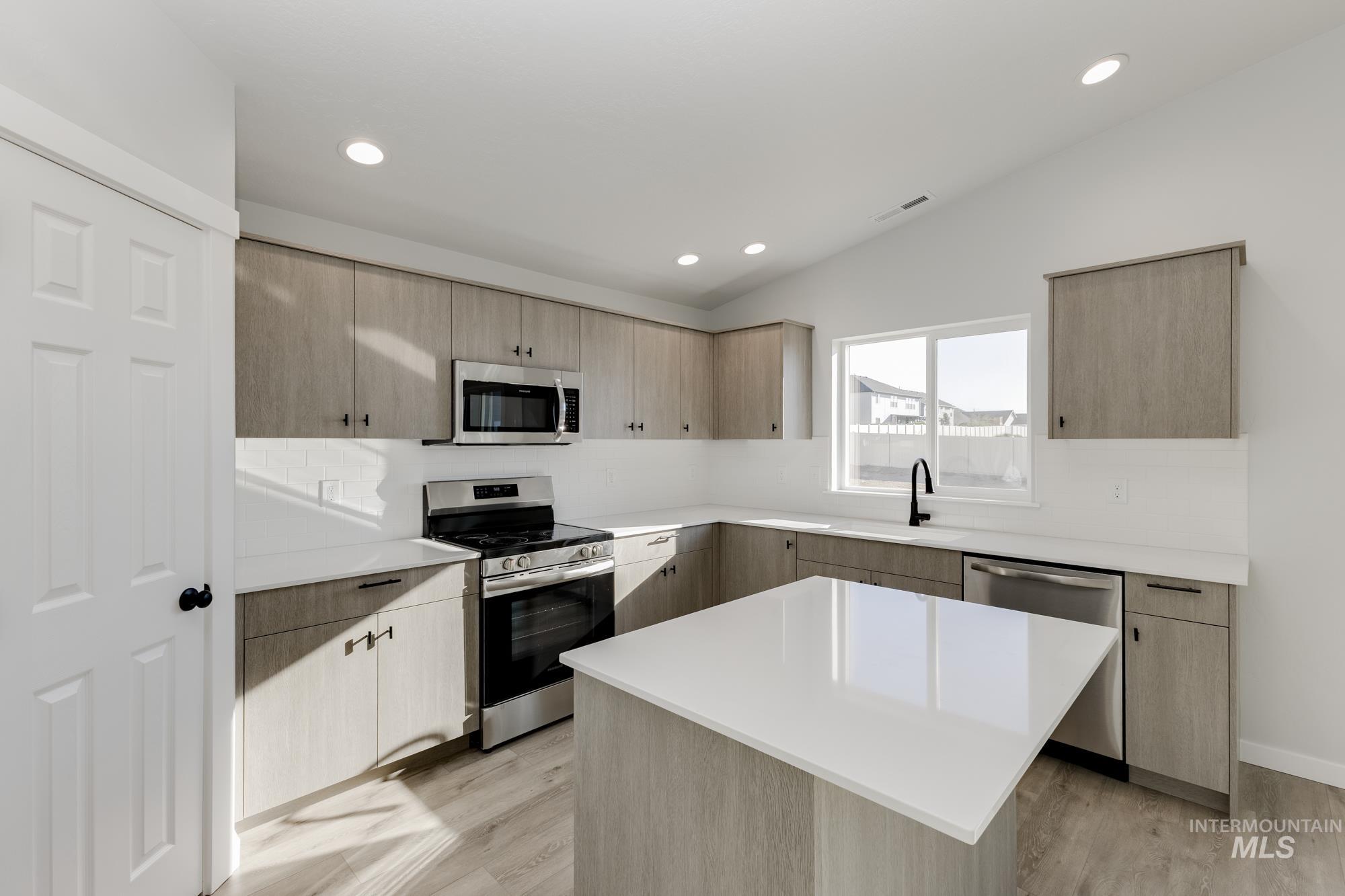 Kitchen with light brown cabinets, stainless steel appliances, a kitchen island, modern cabinets, and vaulted ceiling