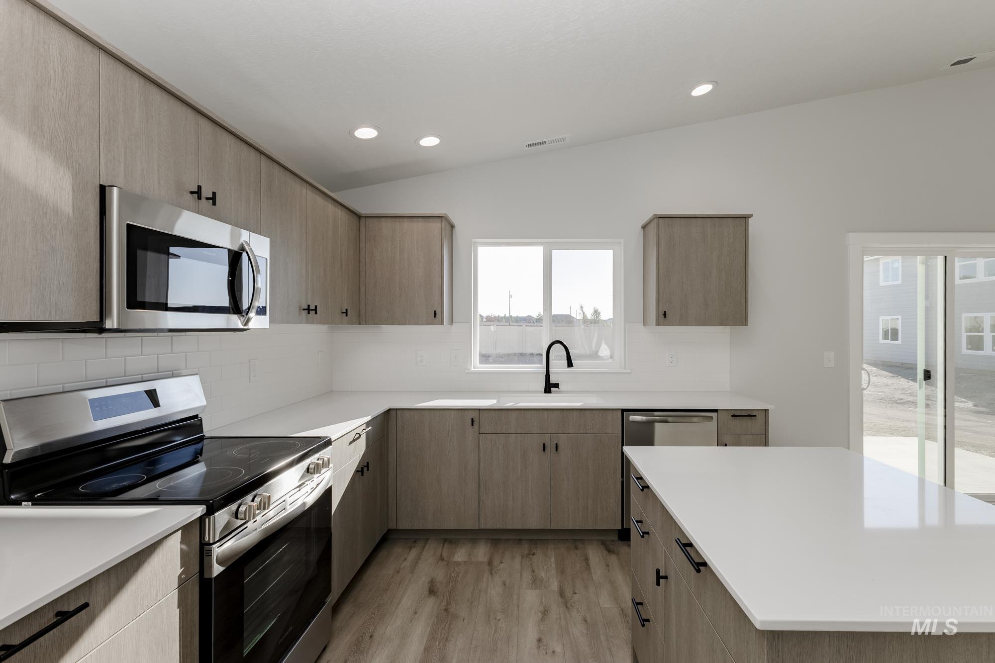 Kitchen with appliances with stainless steel finishes, vaulted ceiling, decorative backsplash, light wood-style flooring, and light brown cabinets