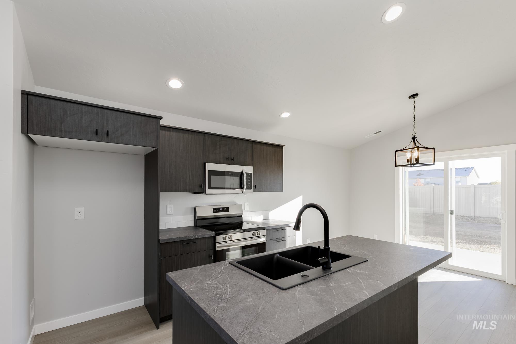 Kitchen featuring stainless steel appliances, dark countertops, a center island with sink, recessed lighting, and light wood finished floors