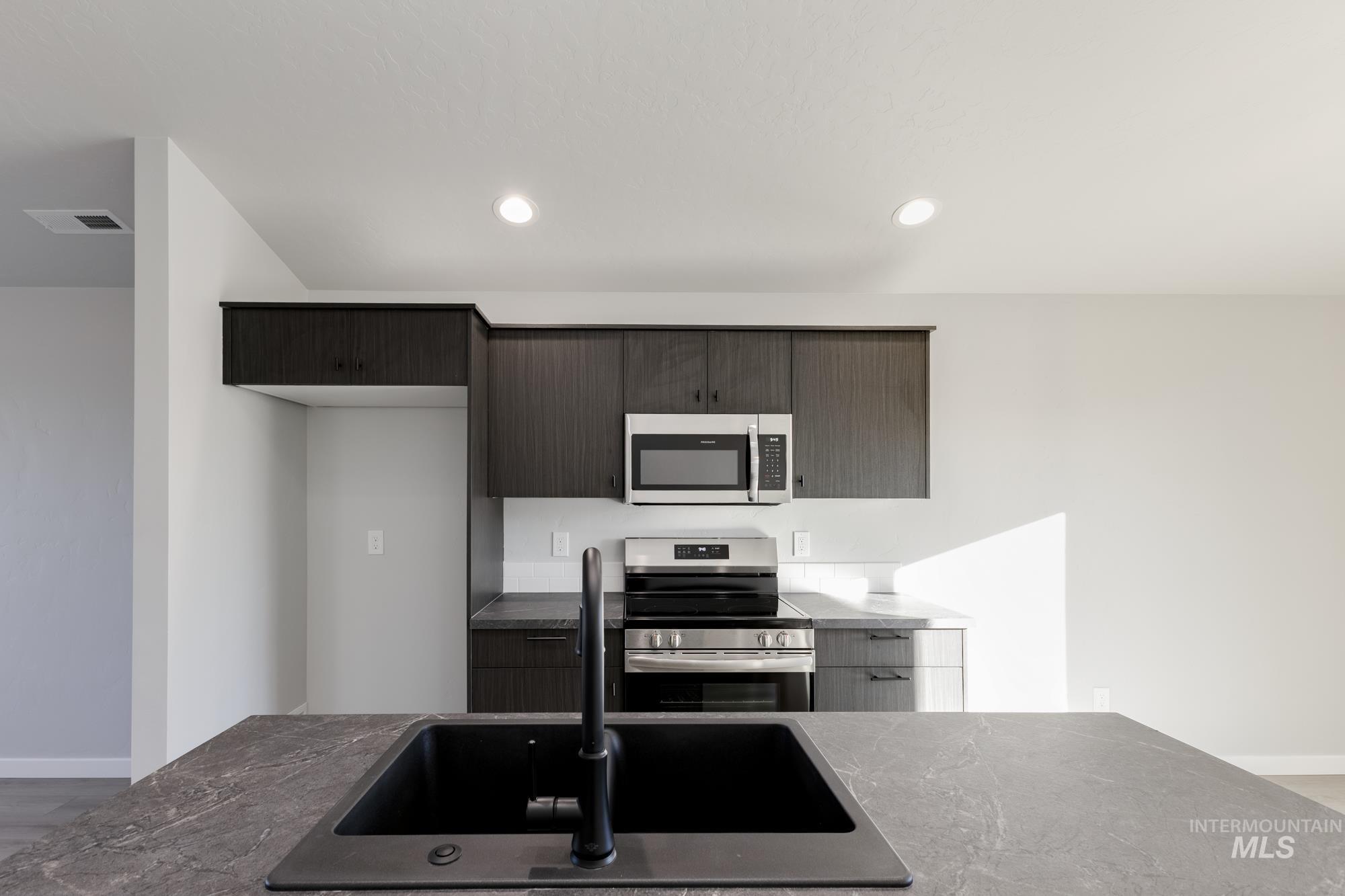 Kitchen with appliances with stainless steel finishes, modern cabinets, recessed lighting, and dark stone counters