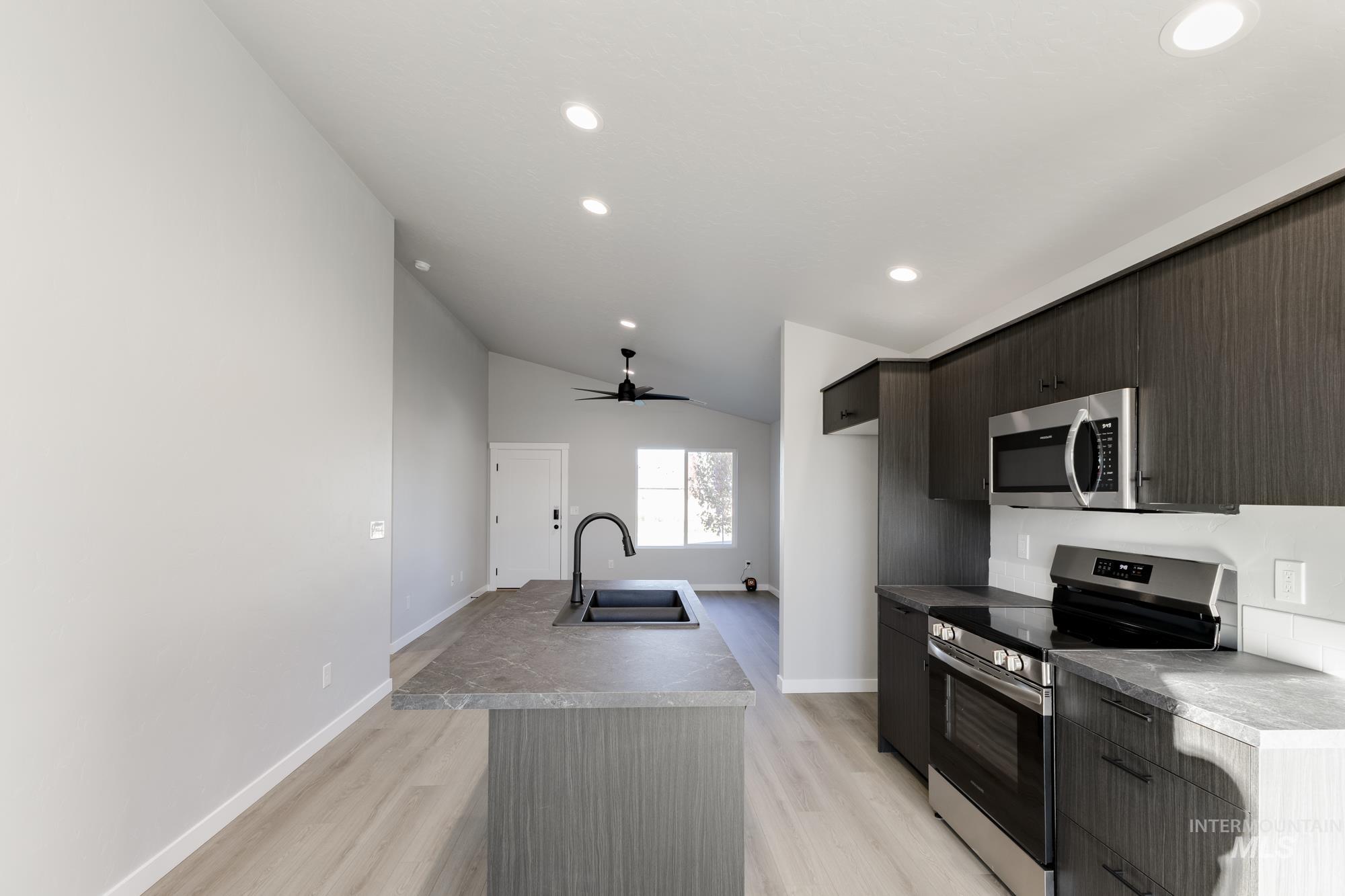 Kitchen with stainless steel appliances, an island with sink, modern cabinets, ceiling fan, and lofted ceiling