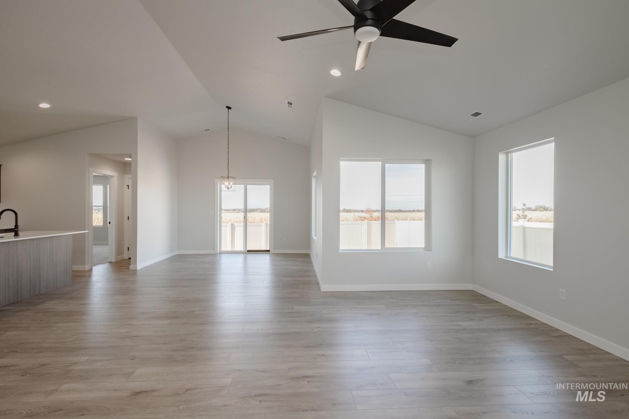 Unfurnished living room featuring lofted ceiling, light wood finished floors, recessed lighting, a chandelier, and a ceiling fan