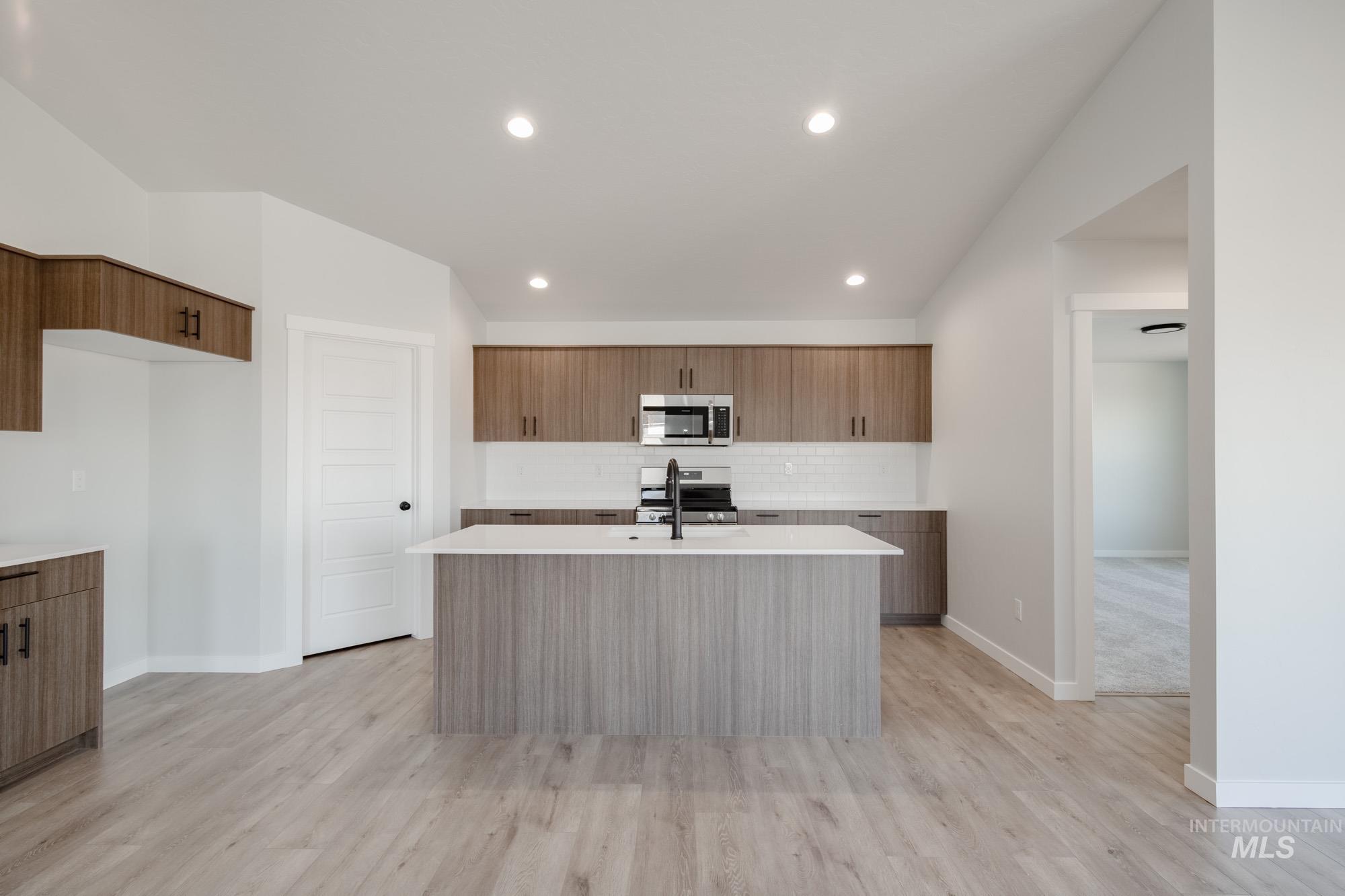Kitchen with modern cabinets, a center island with sink, stainless steel appliances, light stone counters, and recessed lighting