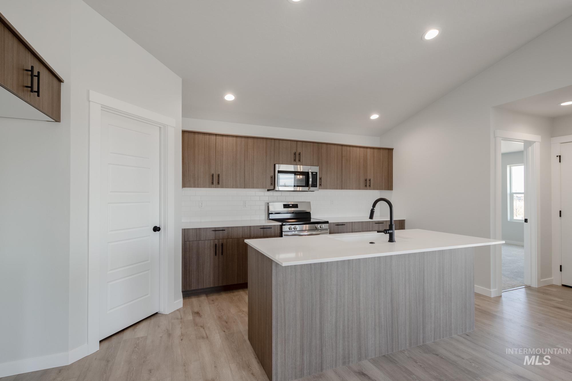 Kitchen featuring modern cabinets, stainless steel appliances, an island with sink, light wood-style floors, and light stone counters