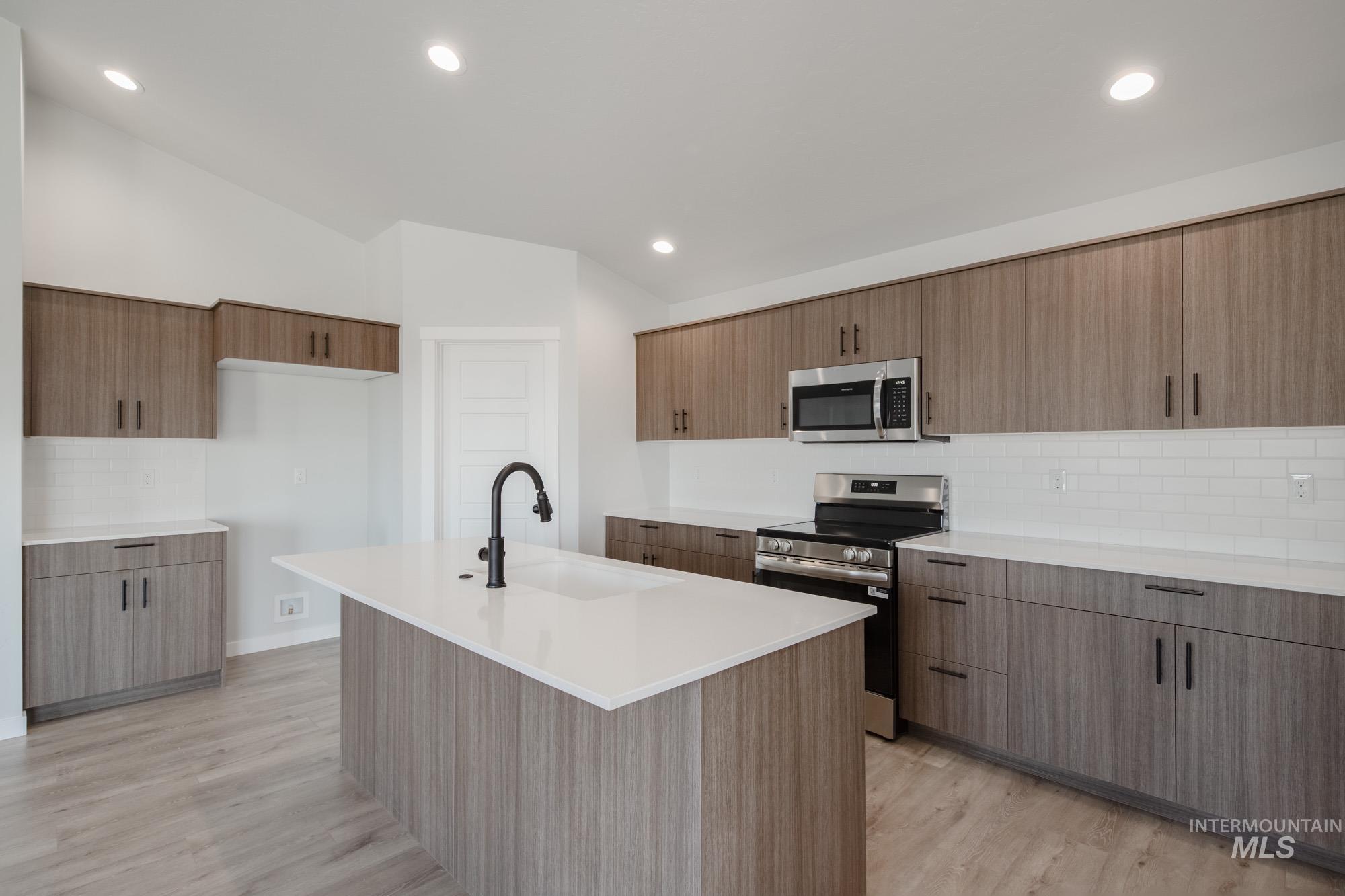 Kitchen with backsplash, stainless steel appliances, light wood finished floors, recessed lighting, and lofted ceiling