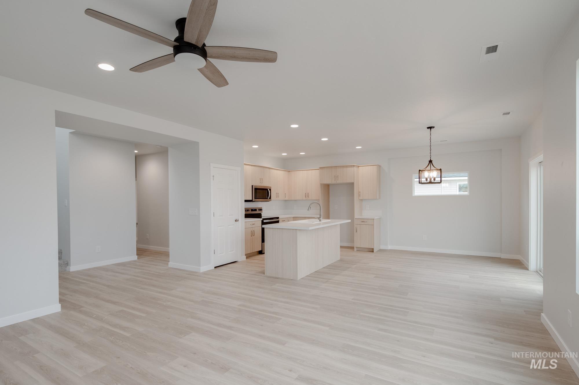 Kitchen with open floor plan, a kitchen island with sink, light wood-type flooring, light countertops, and stainless steel appliances