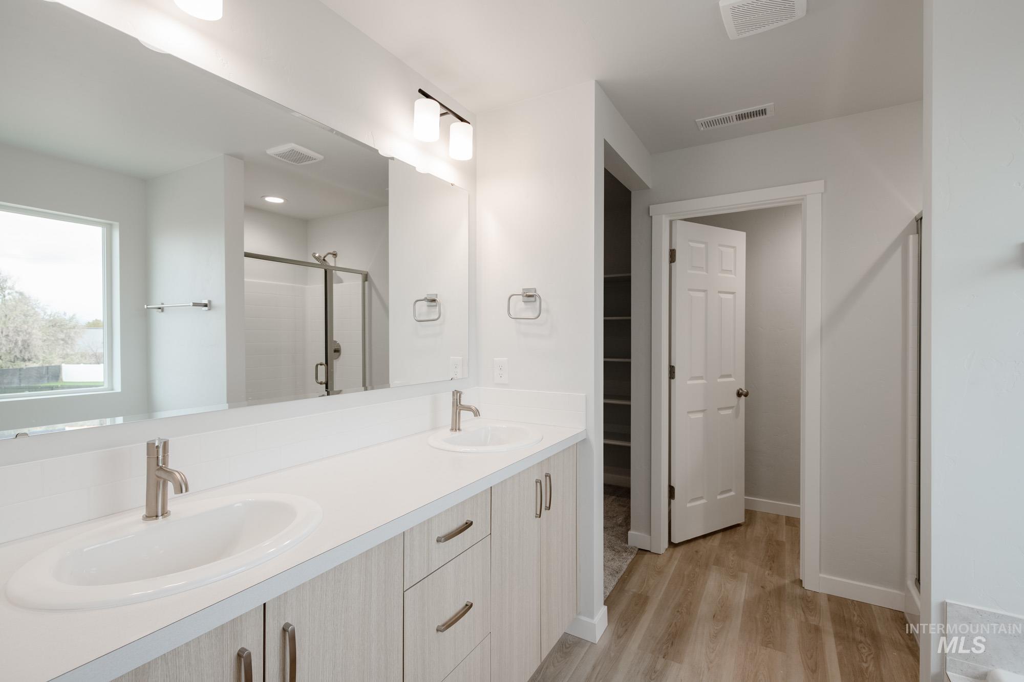Full bath featuring a shower stall, double vanity, light wood finished floors, and a walk in closet