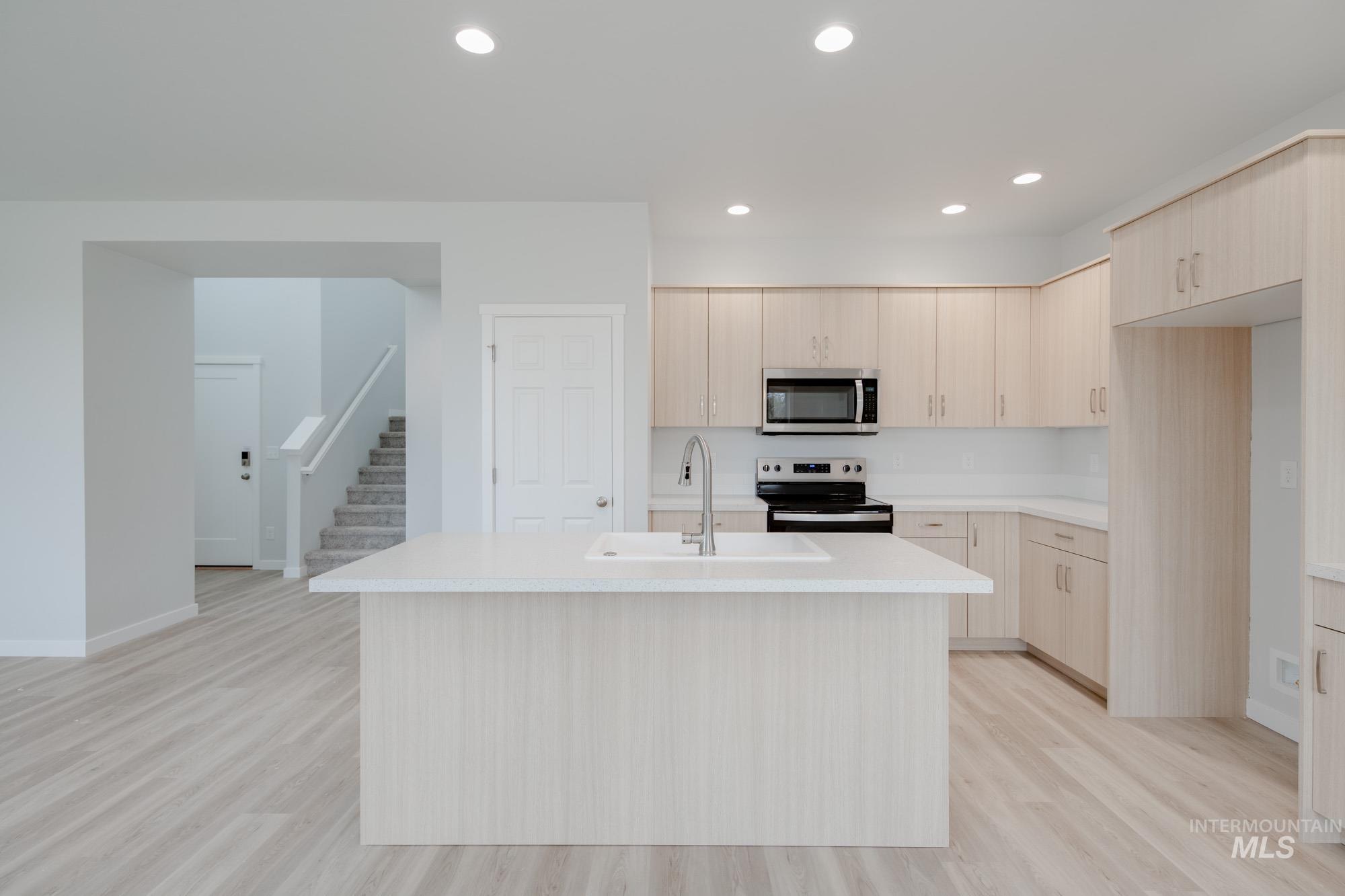 Kitchen featuring light brown cabinets, stainless steel appliances, recessed lighting, light wood-type flooring, and a center island with sink
