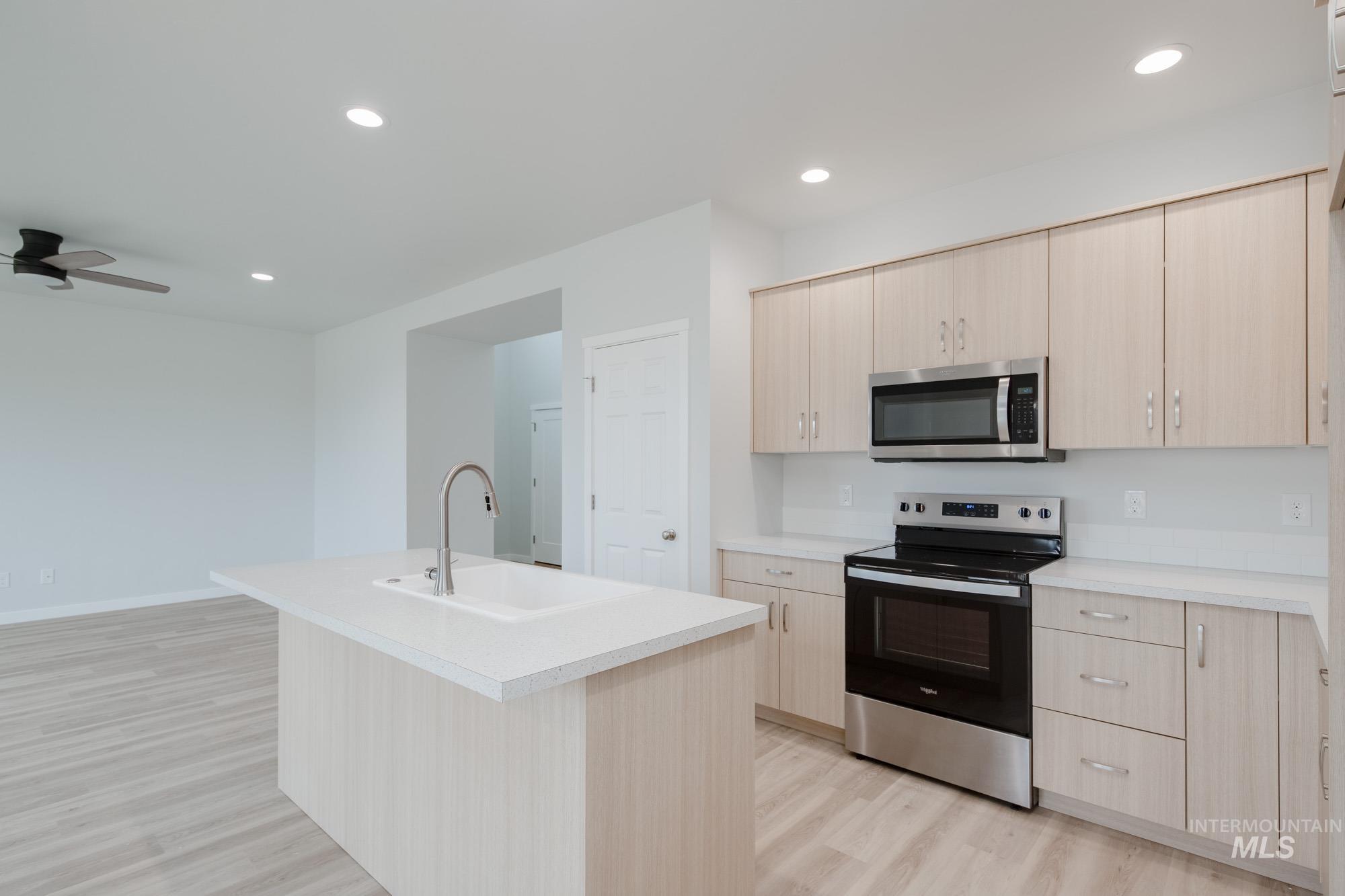 Kitchen featuring light brown cabinetry, stainless steel appliances, light countertops, recessed lighting, and light wood-type flooring