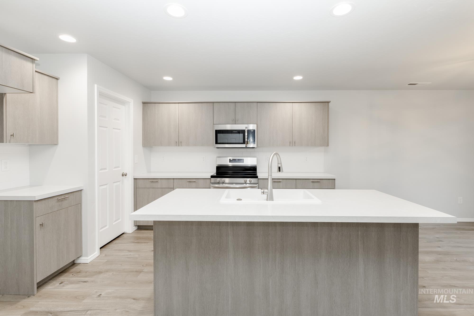 Kitchen featuring light brown cabinetry, appliances with stainless steel finishes, a center island with sink, light wood-style floors, and recessed lighting