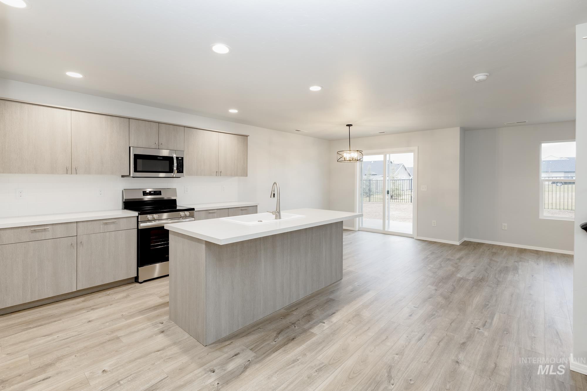 Kitchen featuring light brown cabinets, appliances with stainless steel finishes, pendant lighting, light wood-style floors, and recessed lighting