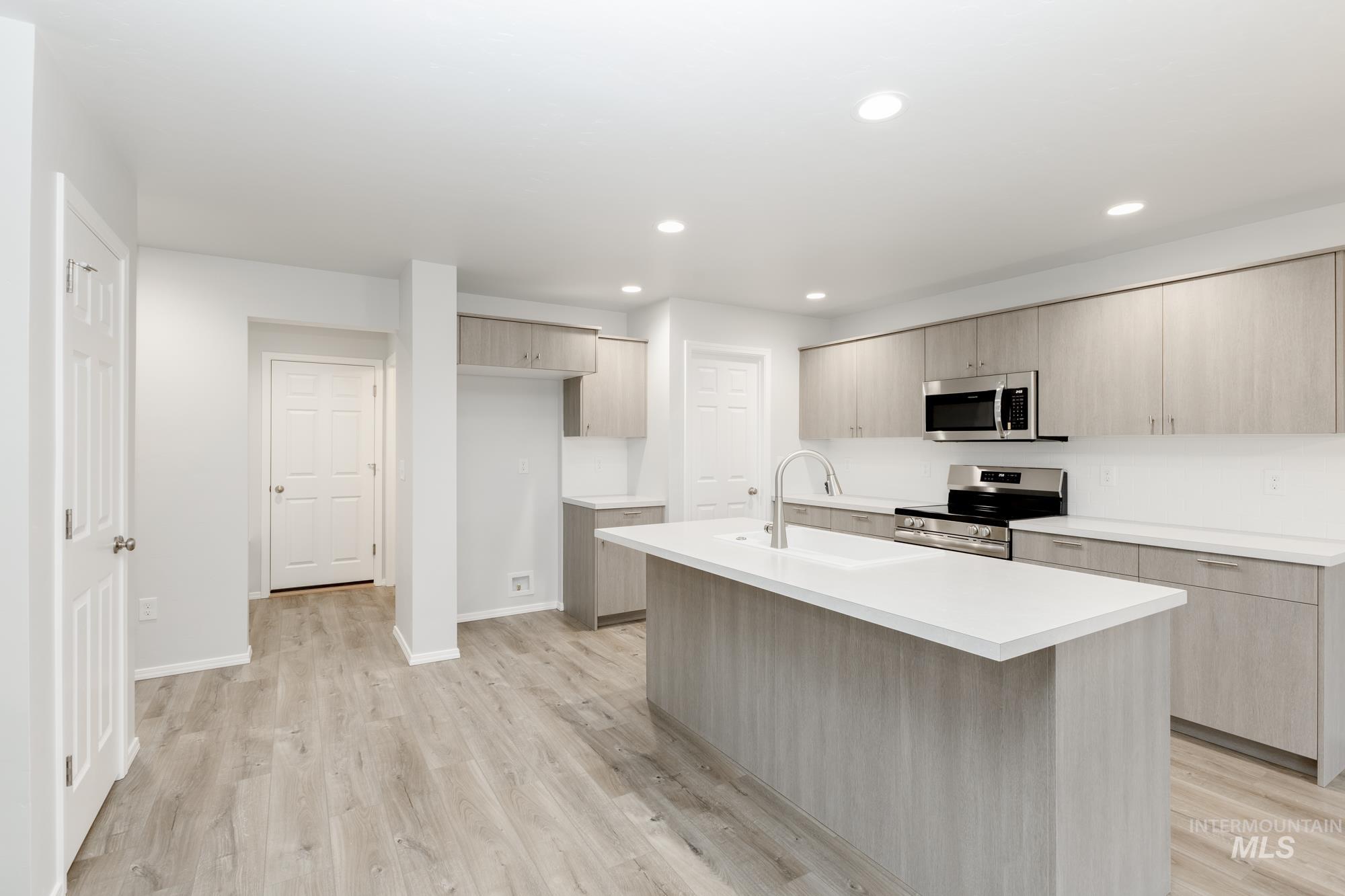 Kitchen with light countertops, appliances with stainless steel finishes, light wood finished floors, an island with sink, and recessed lighting