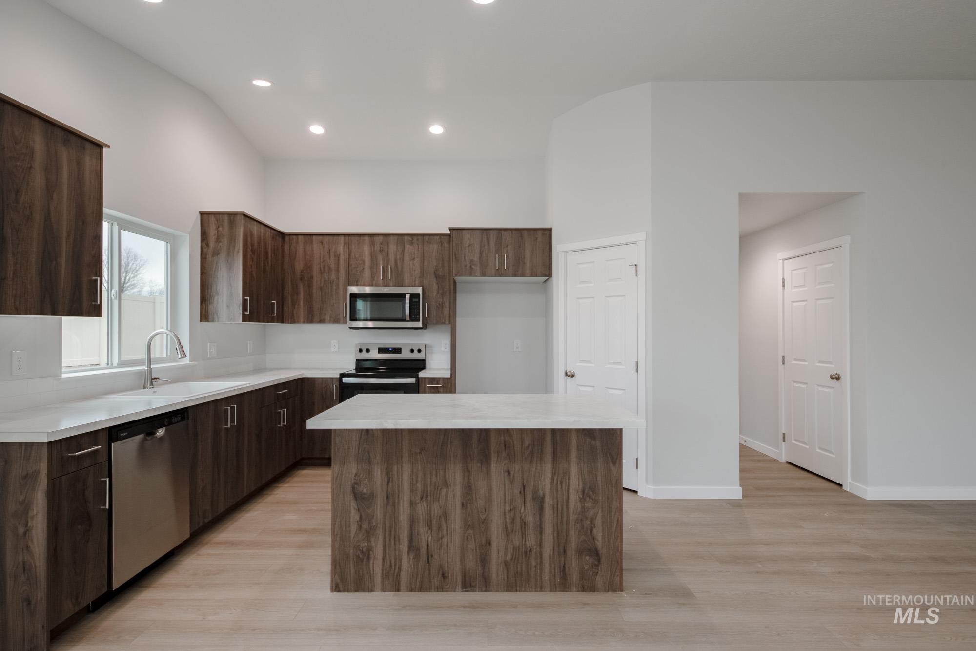 Kitchen featuring appliances with stainless steel finishes, modern cabinets, dark brown cabinets, light wood-style flooring, and a kitchen island