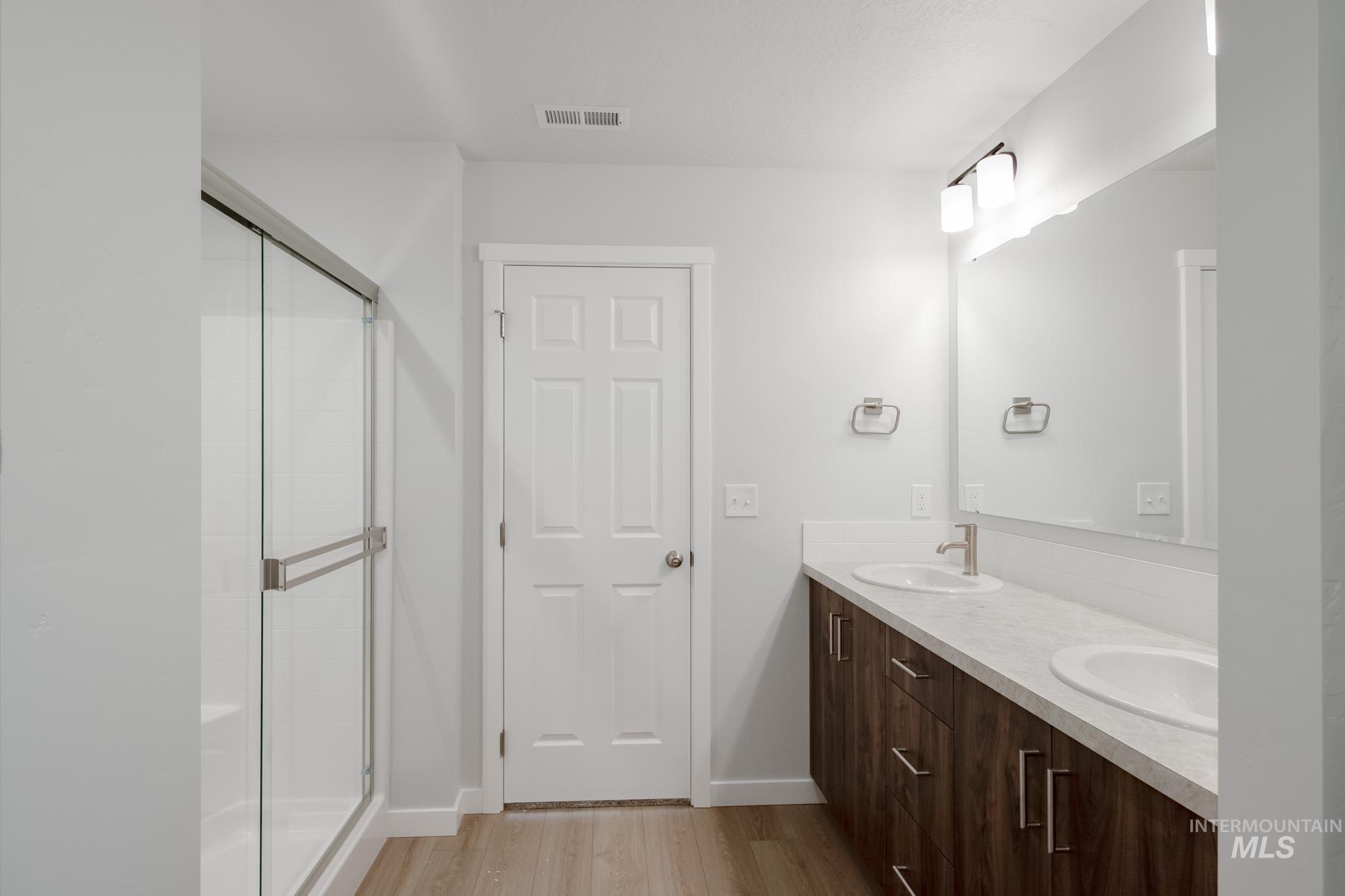 Full bath featuring double vanity, light wood finished floors, and a stall shower