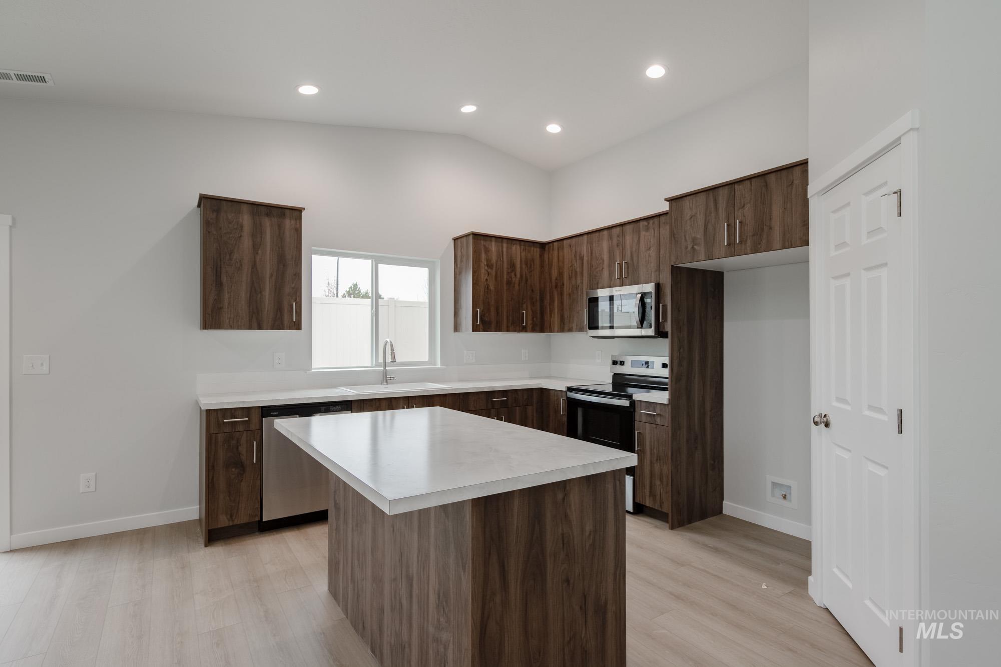 Kitchen with dark brown cabinetry, light countertops, appliances with stainless steel finishes, light wood-style floors, and a kitchen island