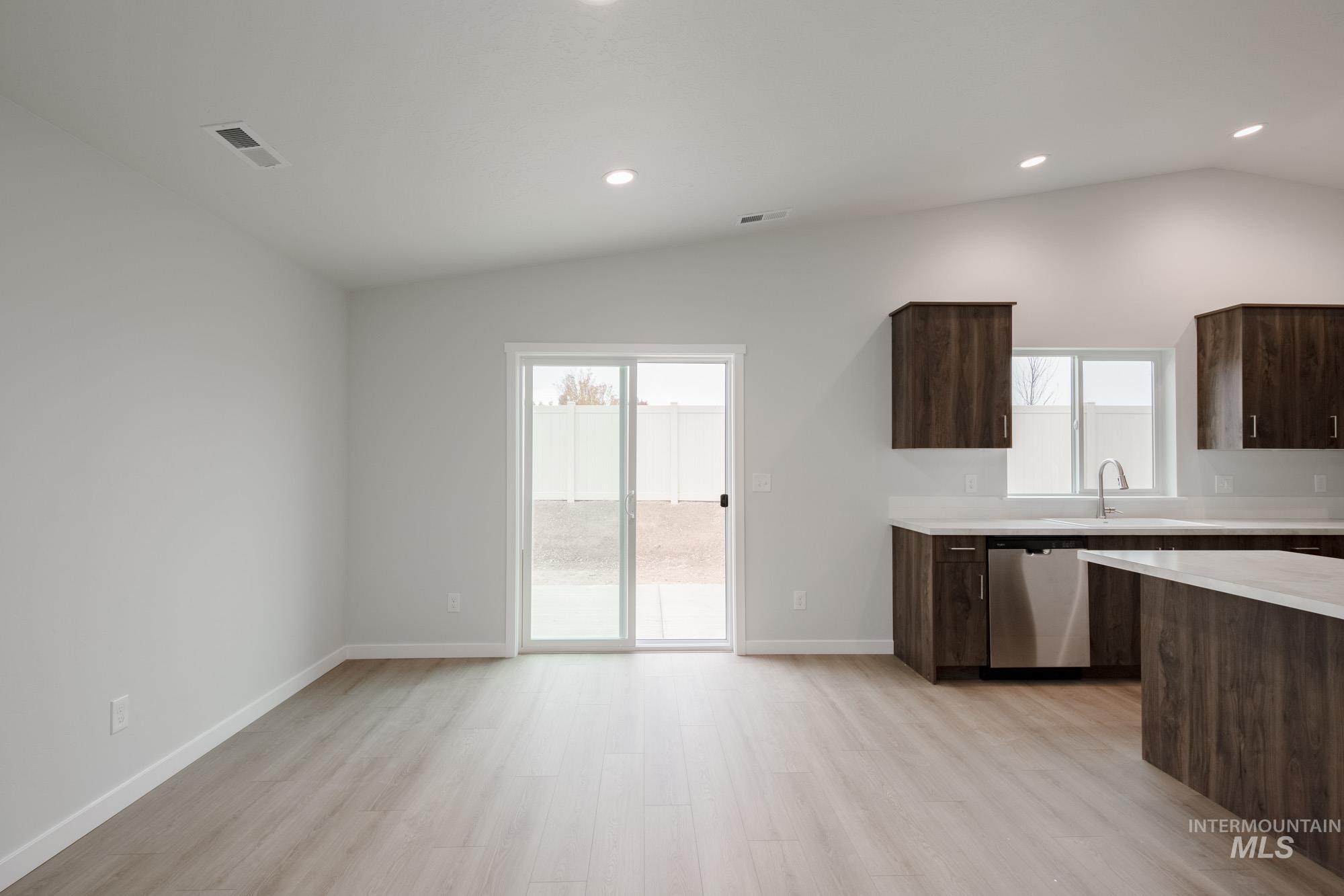 Kitchen featuring dark brown cabinets, vaulted ceiling, modern cabinets, stainless steel dishwasher, and light wood finished floors