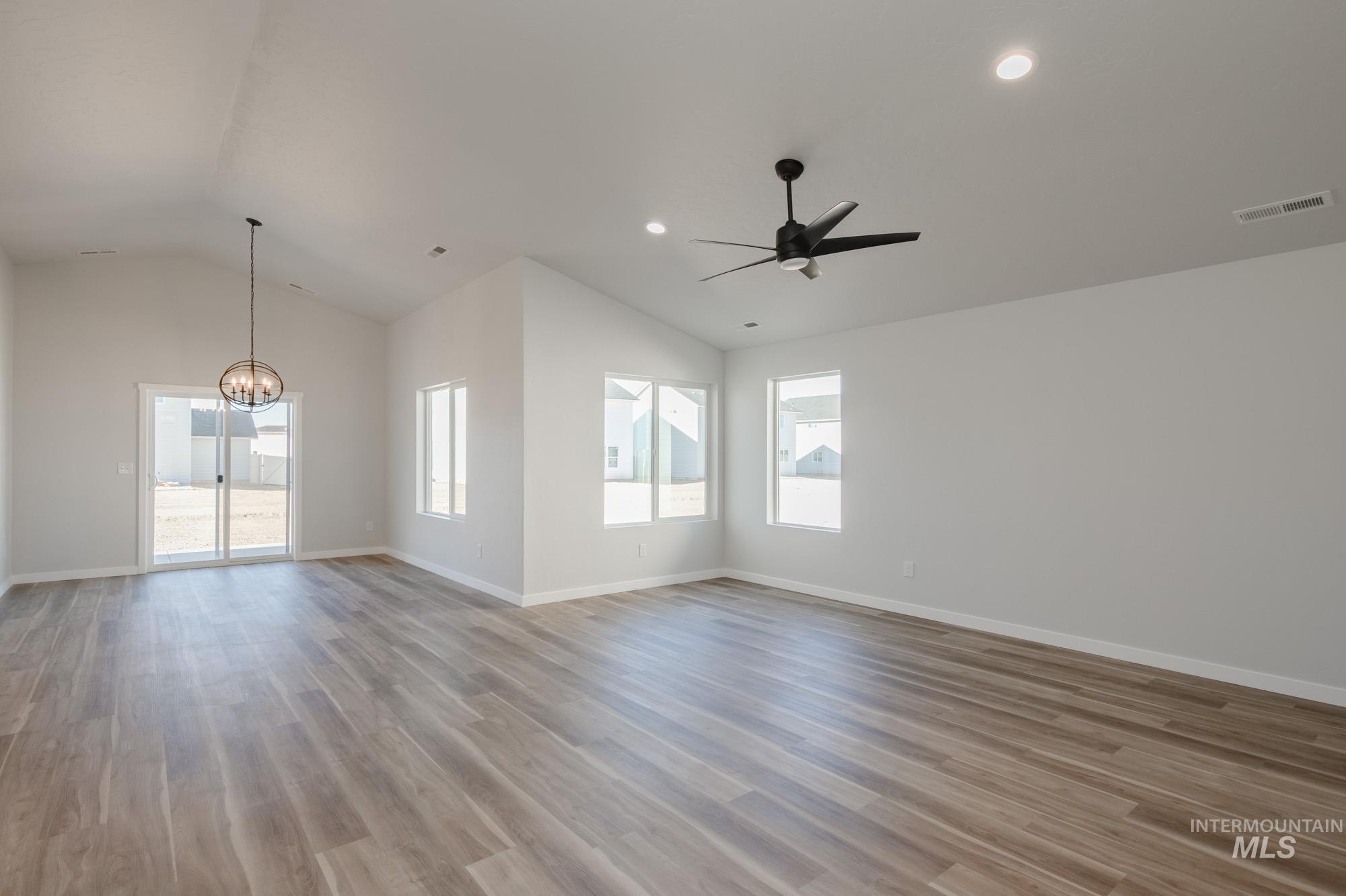 Empty room with lofted ceiling, light wood-type flooring, a ceiling fan, a chandelier, and recessed lighting