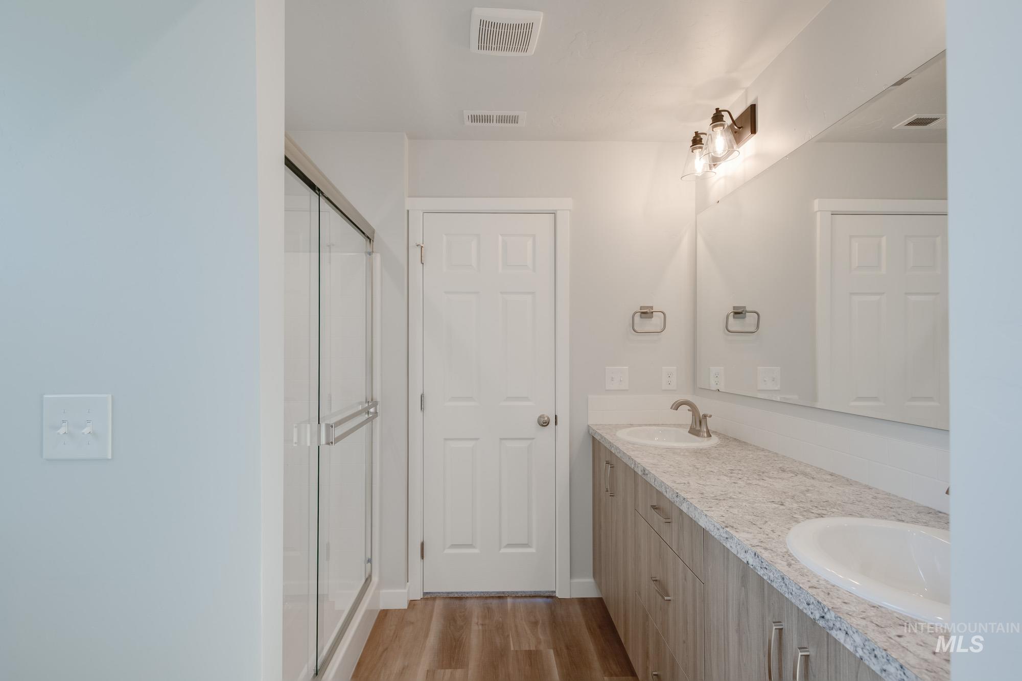 Full bathroom featuring double vanity, light wood-style floors, and a stall shower