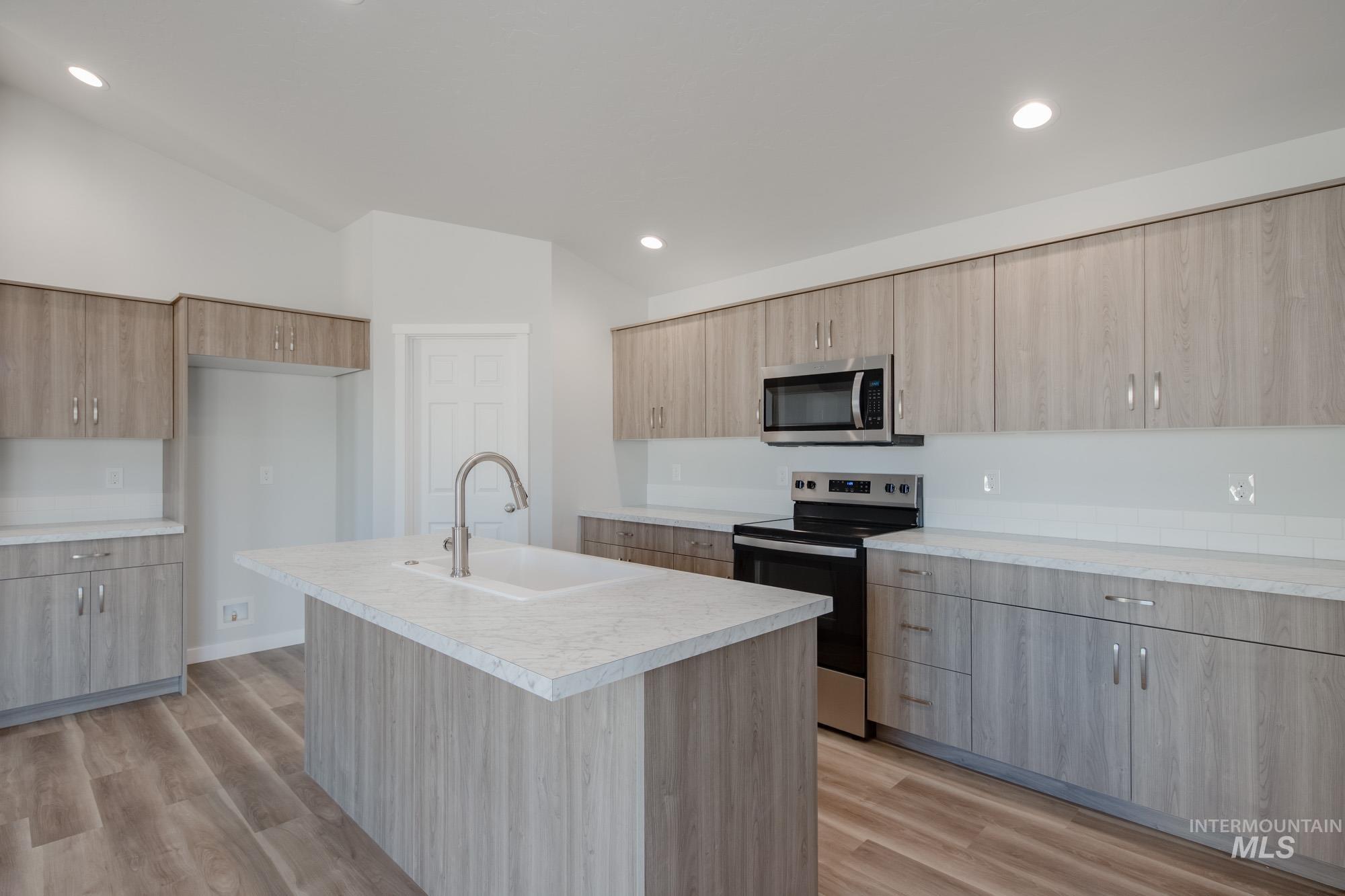 Kitchen with appliances with stainless steel finishes, light countertops, an island with sink, light wood-style floors, and recessed lighting