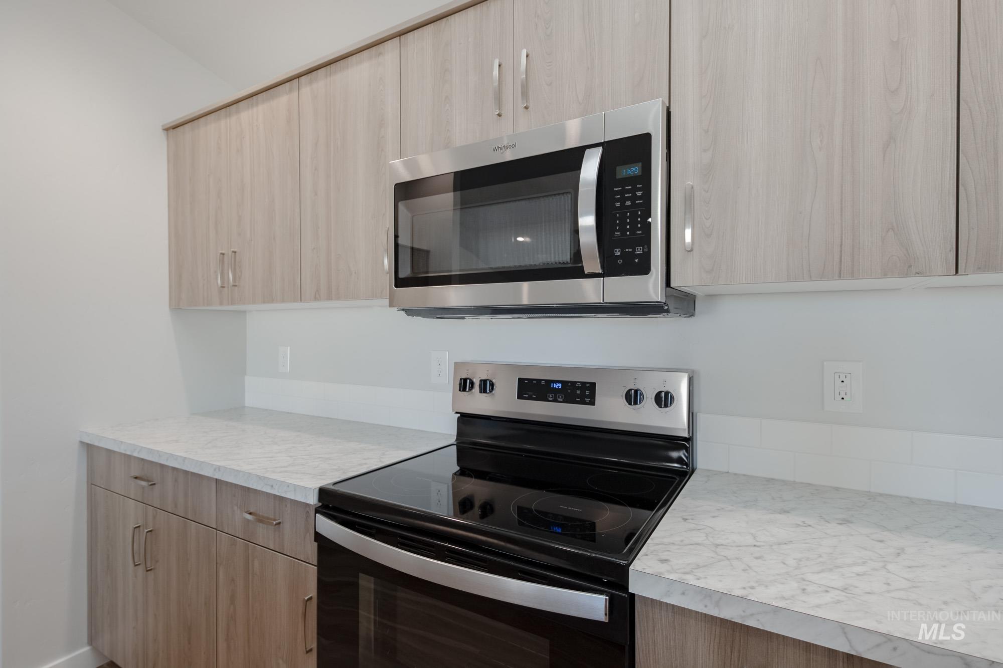 Kitchen featuring electric range oven, stainless steel microwave, light countertops, light brown cabinets, and modern cabinets