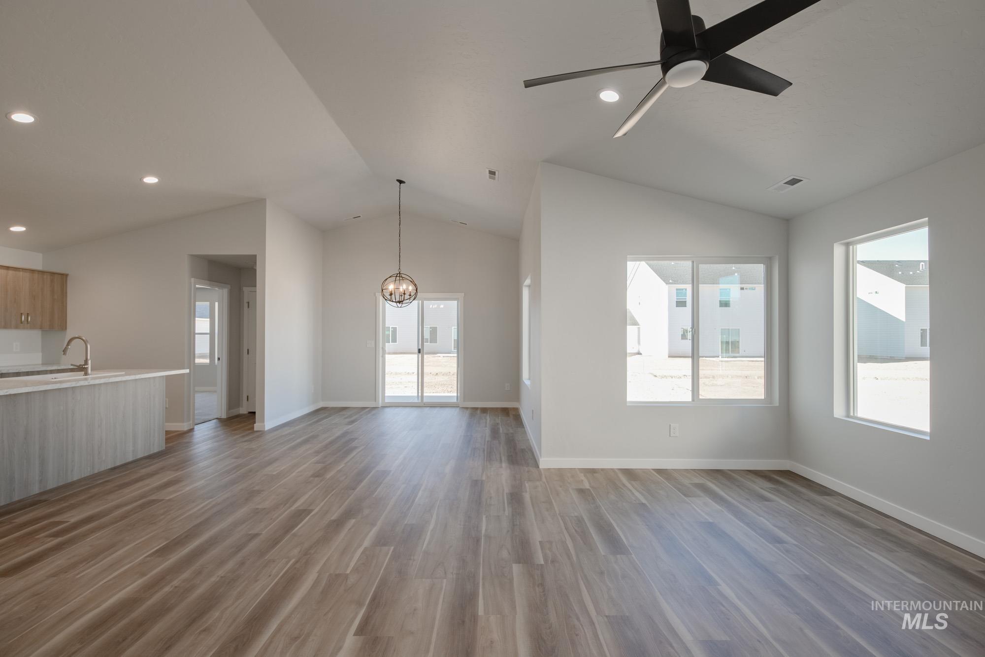 Unfurnished living room with vaulted ceiling, light wood finished floors, a ceiling fan, recessed lighting, and a chandelier