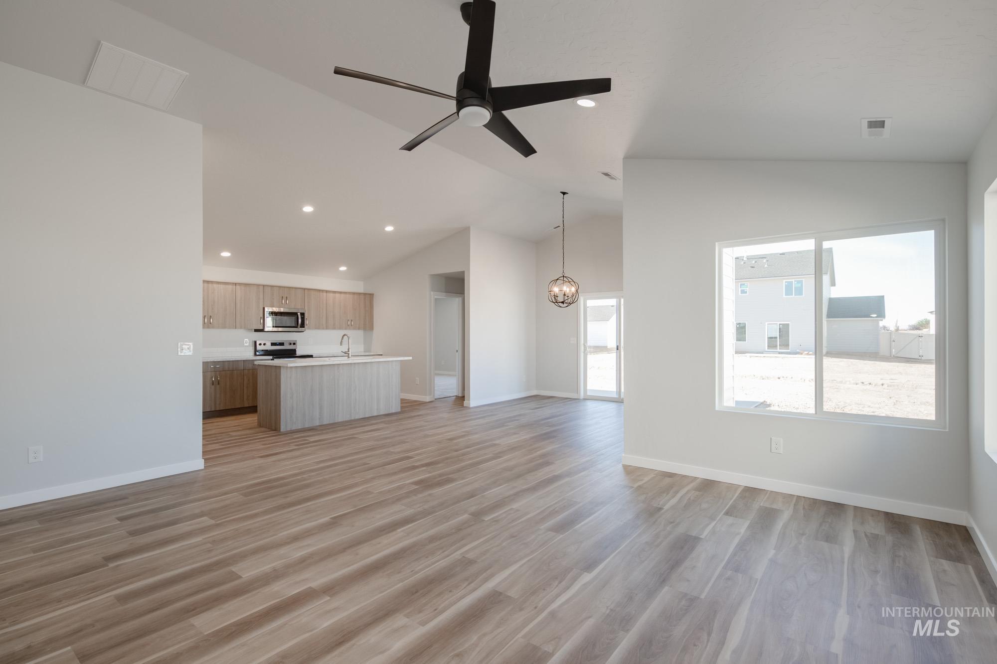 Unfurnished living room featuring vaulted ceiling, ceiling fan, light wood-type flooring, recessed lighting, and a chandelier