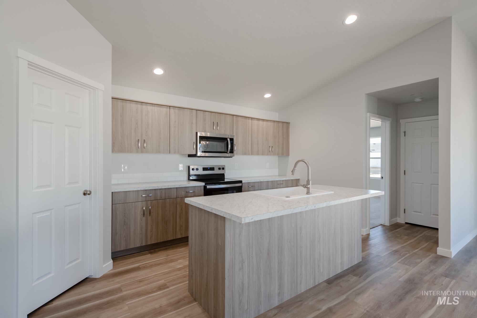 Kitchen featuring an island with sink, light countertops, appliances with stainless steel finishes, light wood finished floors, and modern cabinets