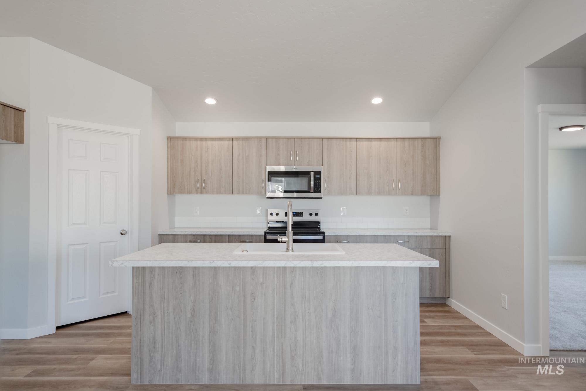 Kitchen featuring light brown cabinets, appliances with stainless steel finishes, an island with sink, modern cabinets, and recessed lighting
