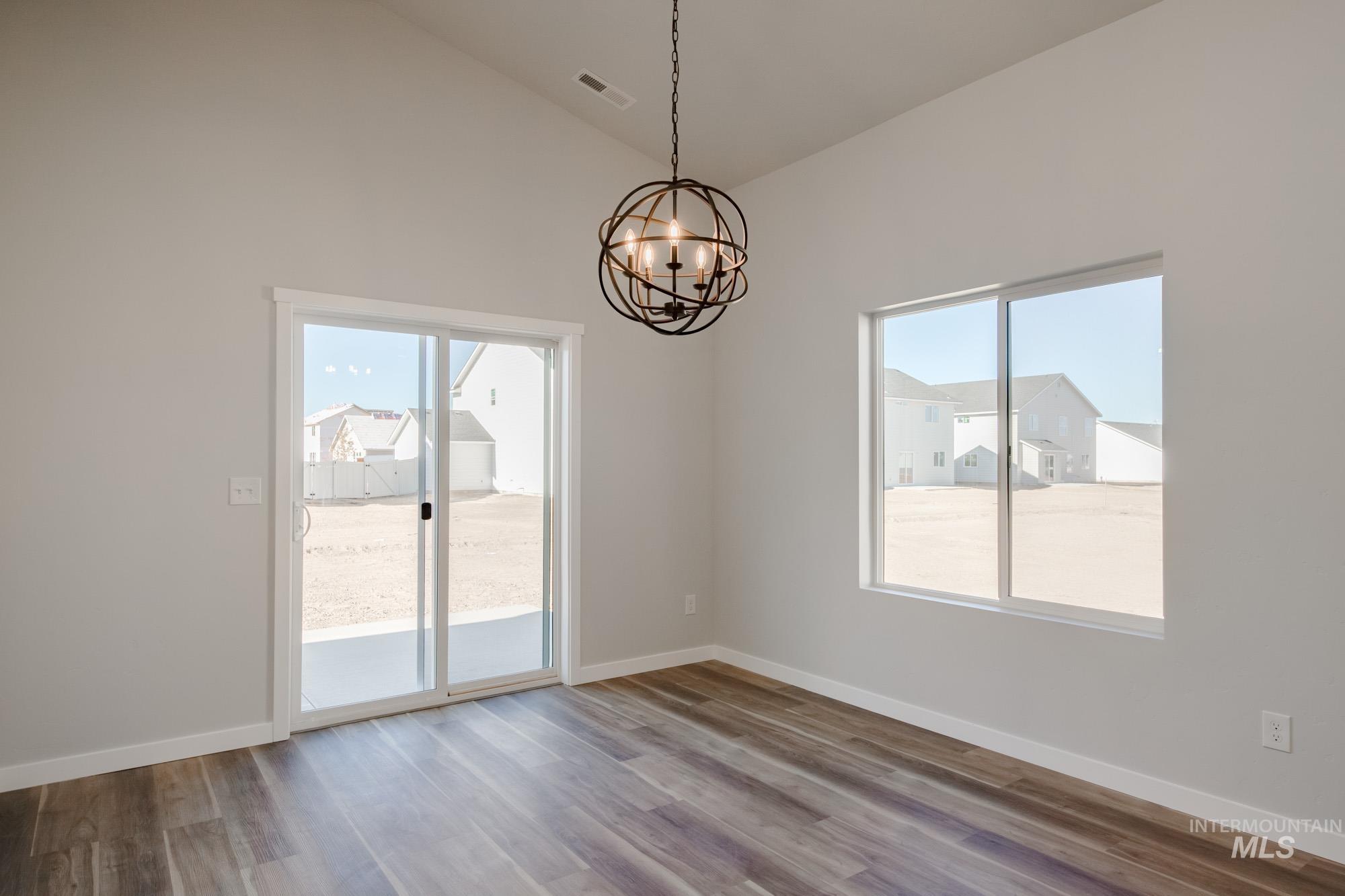 Unfurnished room with plenty of natural light, a chandelier, wood finished floors, and high vaulted ceiling