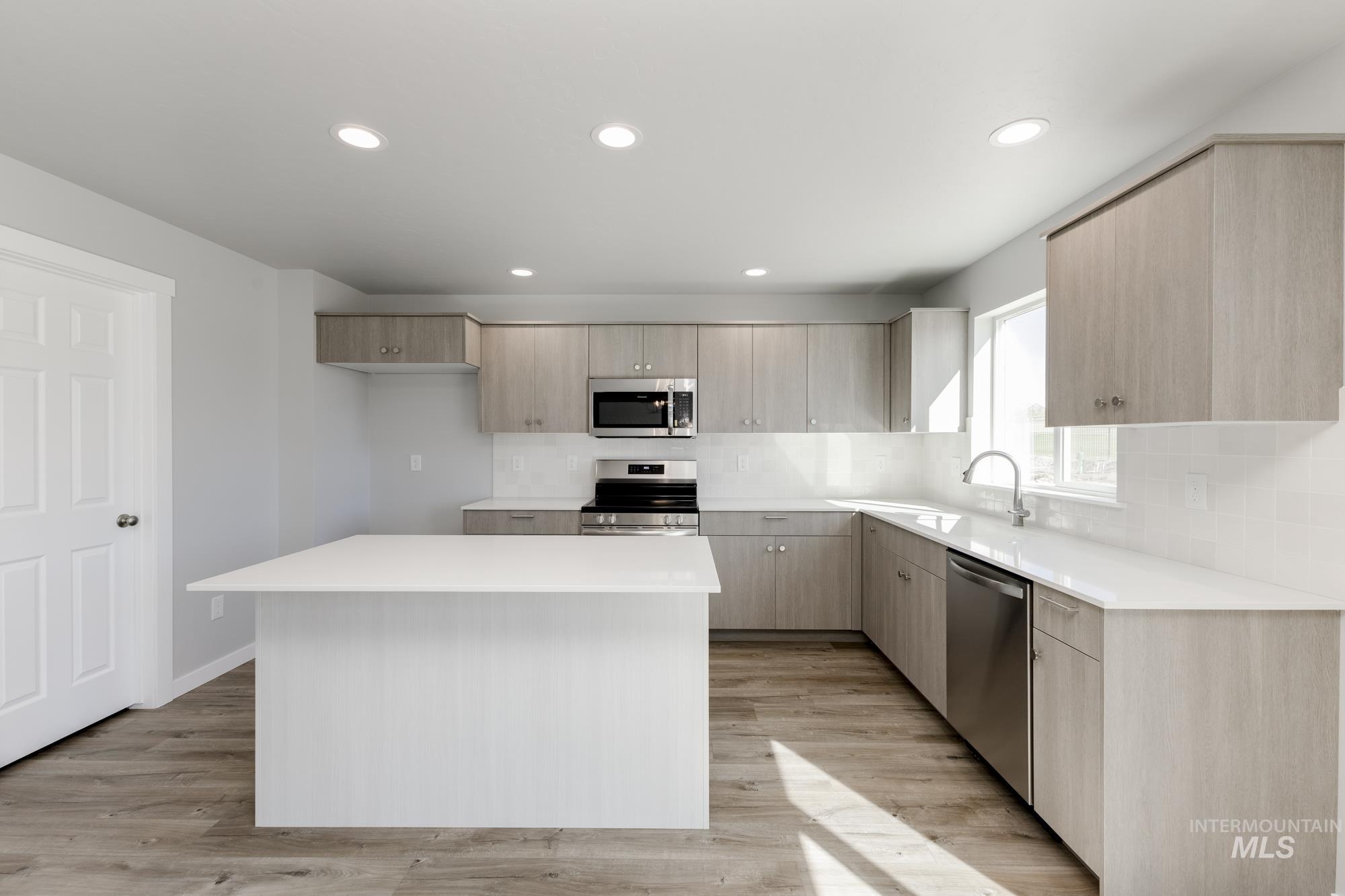 Kitchen featuring light brown cabinetry, a kitchen island, appliances with stainless steel finishes, light wood-style floors, and recessed lighting