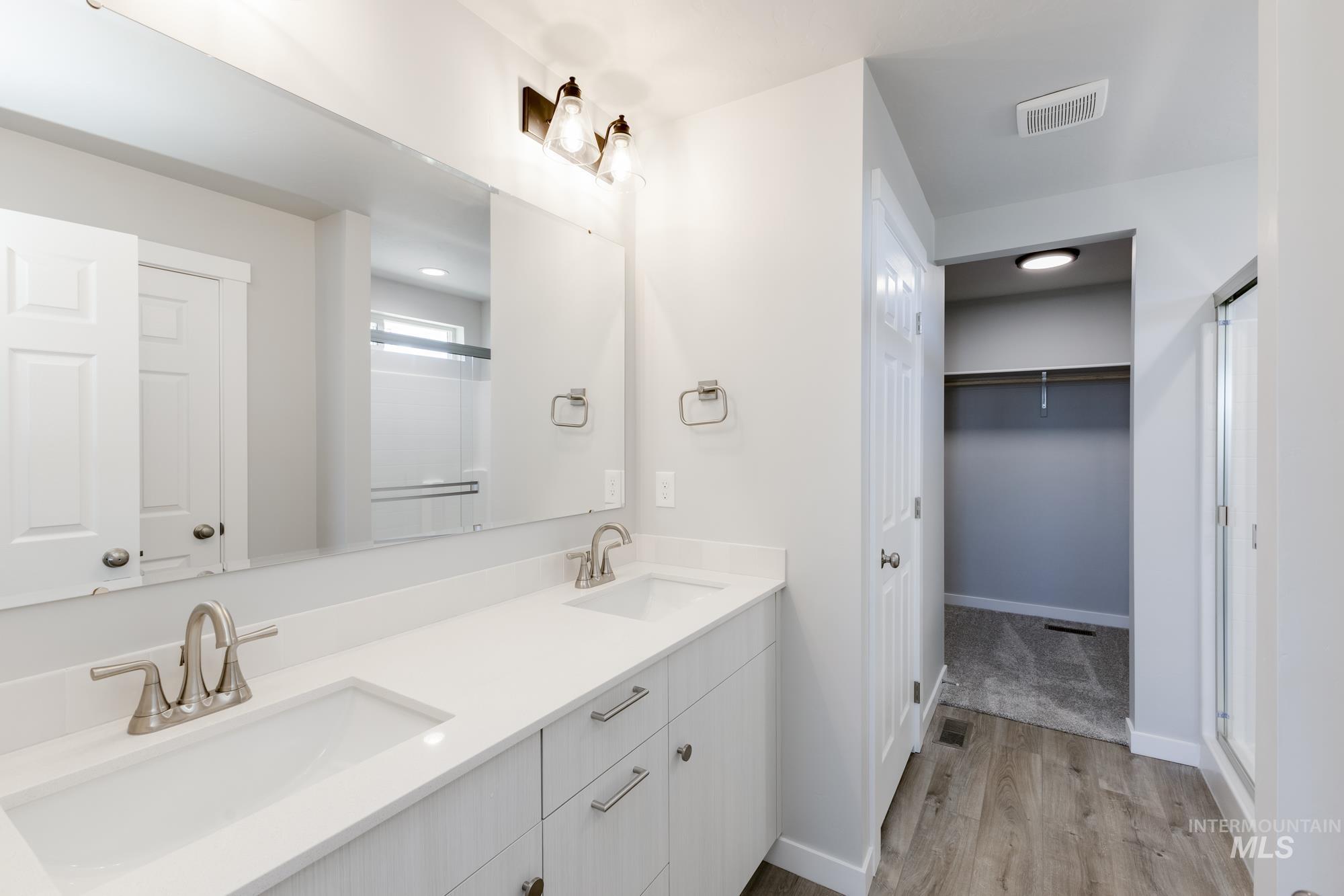 Bathroom featuring a shower stall, a walk in closet, double vanity, and light wood-type flooring