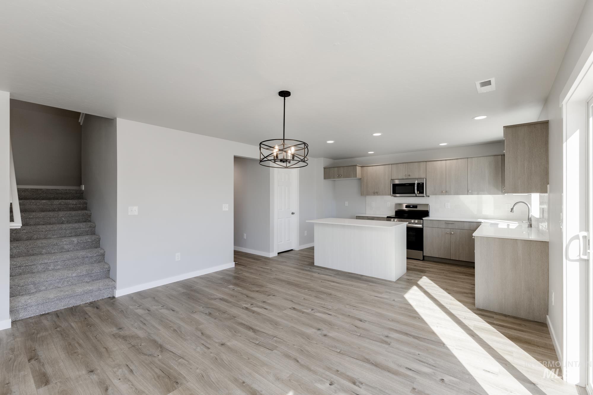Kitchen with a chandelier, appliances with stainless steel finishes, decorative light fixtures, a center island, and light wood-type flooring