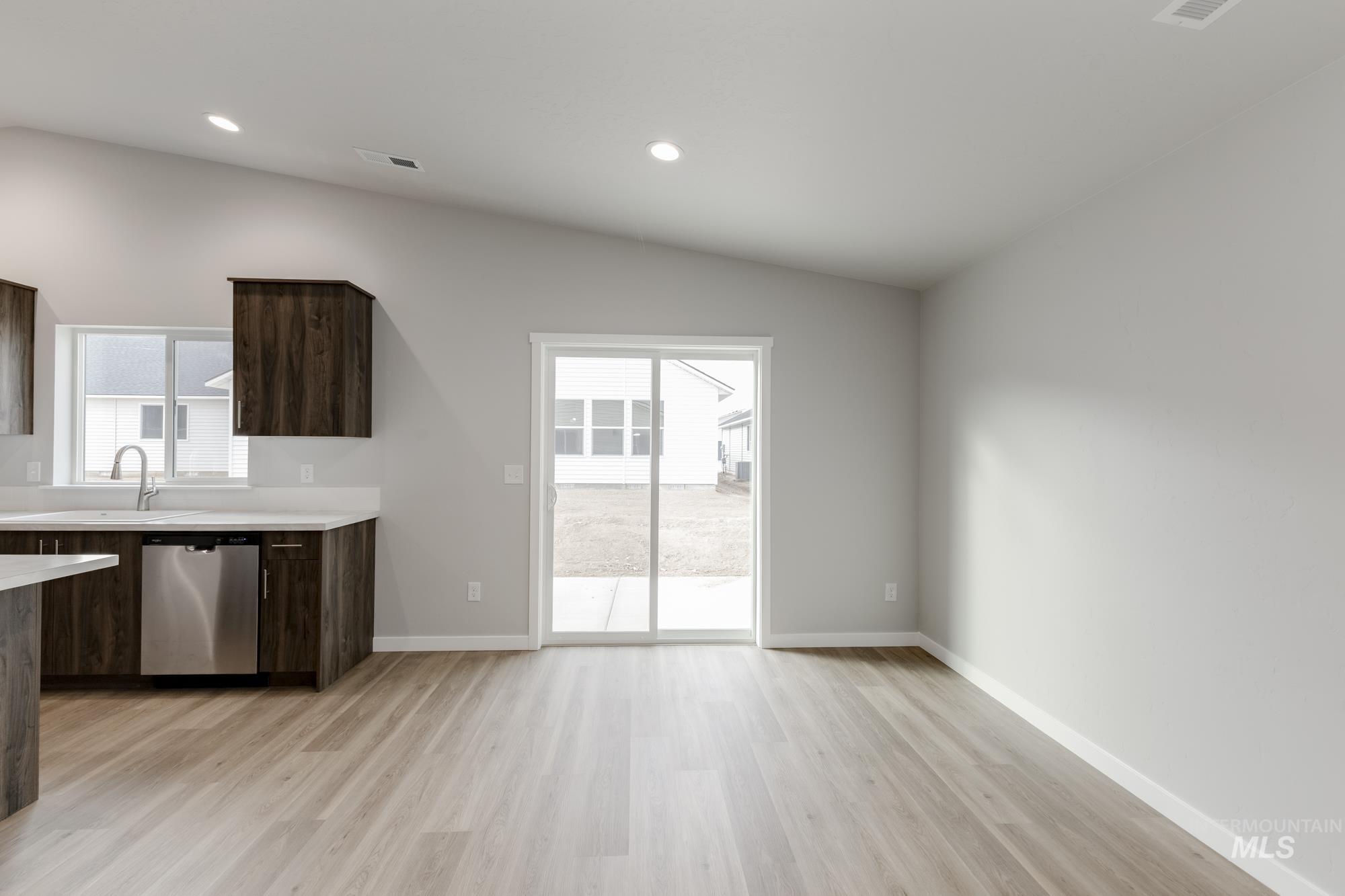 Kitchen with dark brown cabinetry, plenty of natural light, stainless steel dishwasher, light wood finished floors, and lofted ceiling