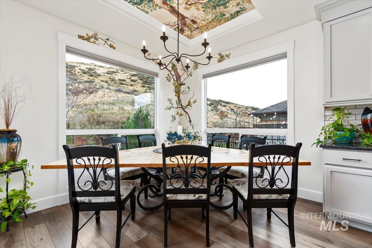 Dining room featuring plenty of natural light, a chandelier, light wood-style flooring, ornamental molding, and a raised ceiling