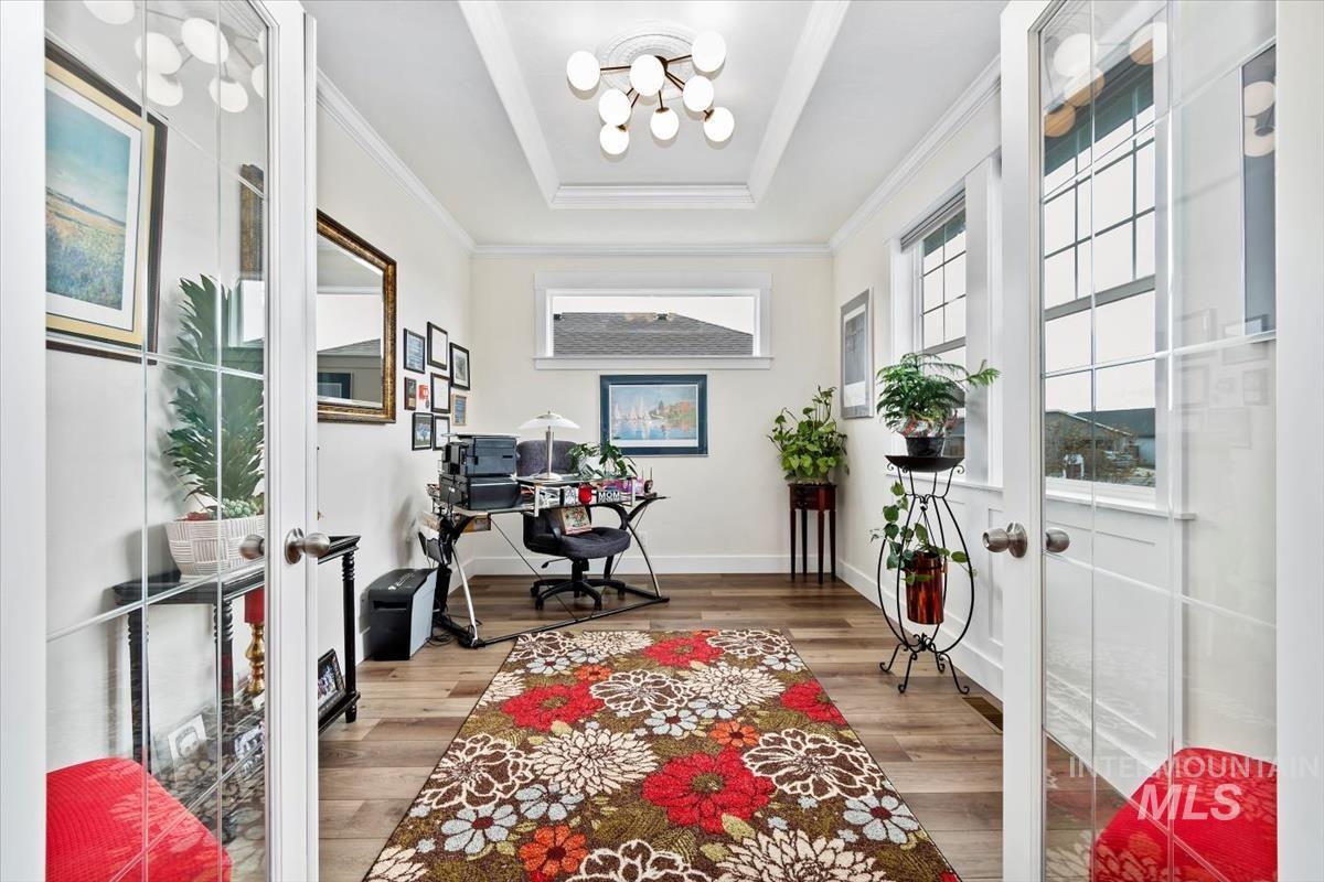 Home office featuring french doors, a chandelier, light wood-style floors, a raised ceiling, and ornamental molding