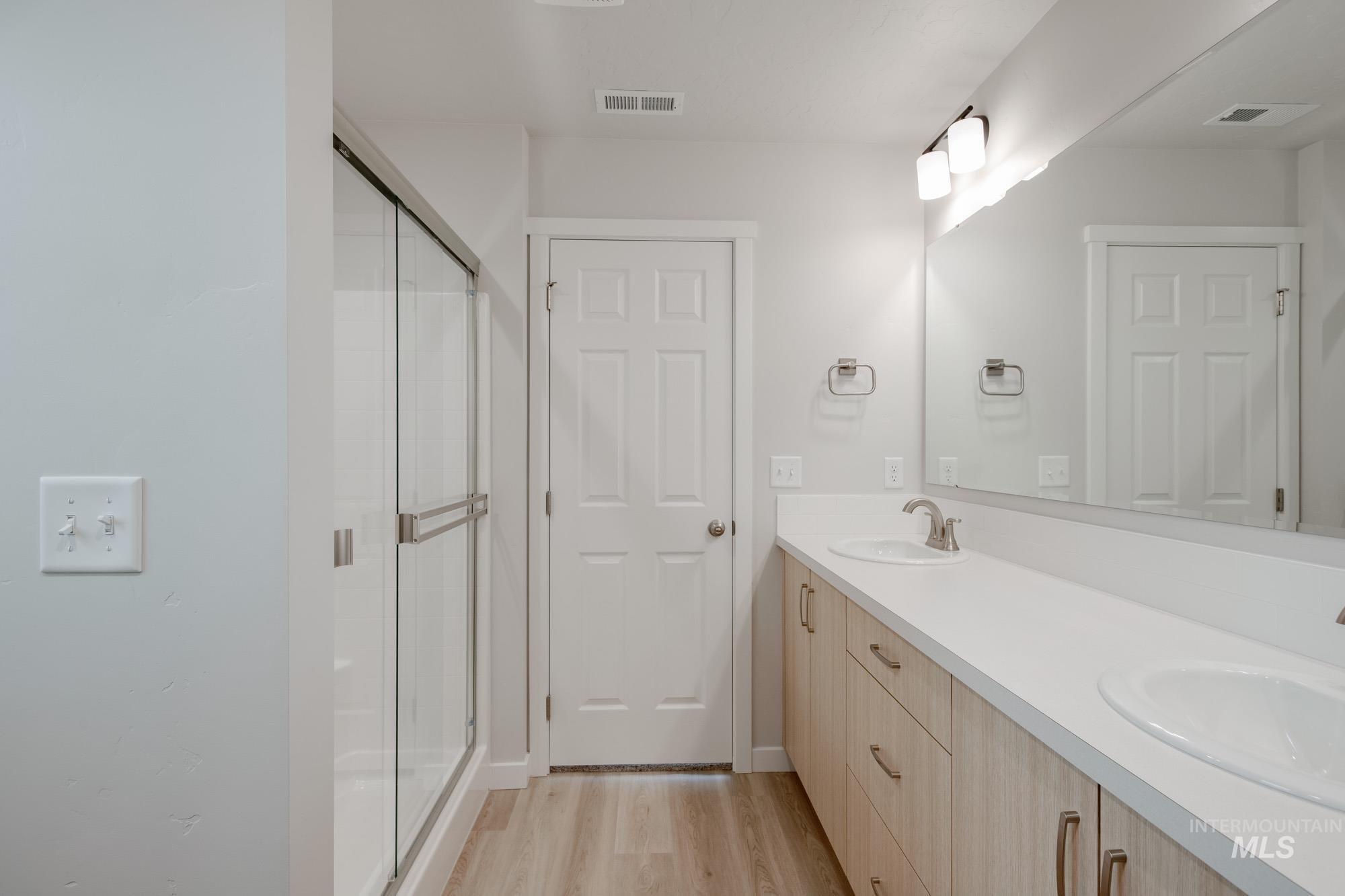 Bathroom with double vanity, light wood-style floors, and a shower stall