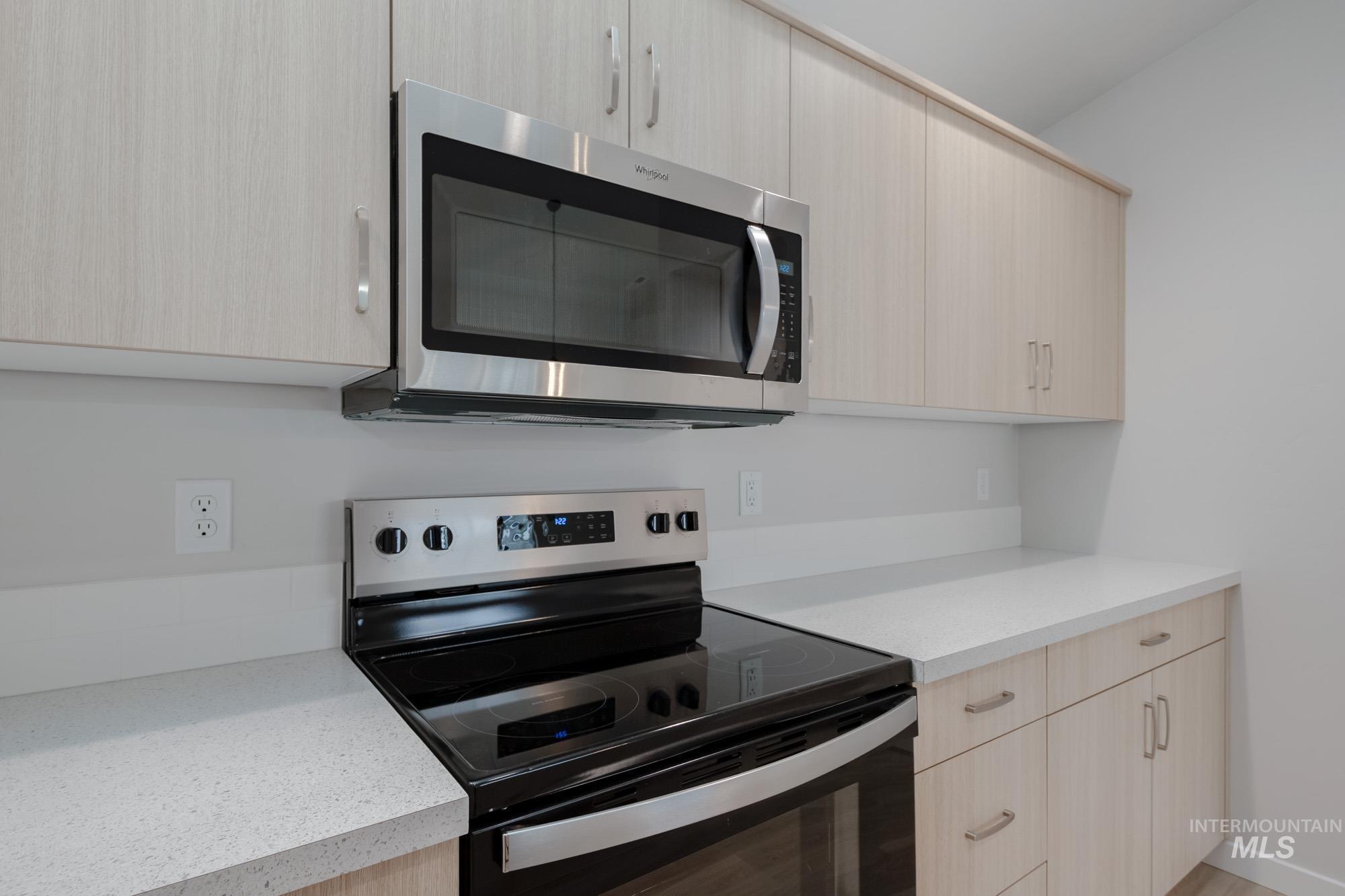 Kitchen featuring stainless steel appliances, light brown cabinetry, modern cabinets, and light stone countertops