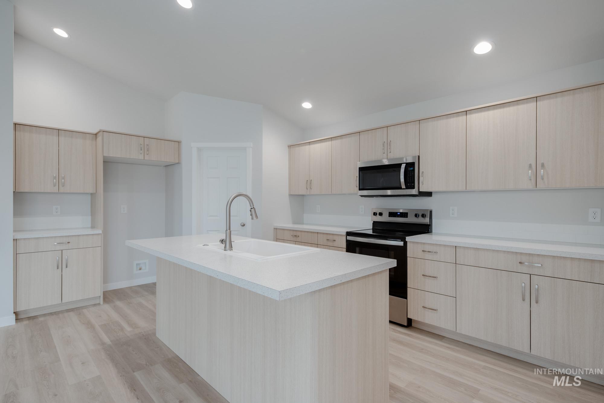 Kitchen featuring range with electric cooktop, light brown cabinets, light wood-style floors, light countertops, and stainless steel microwave