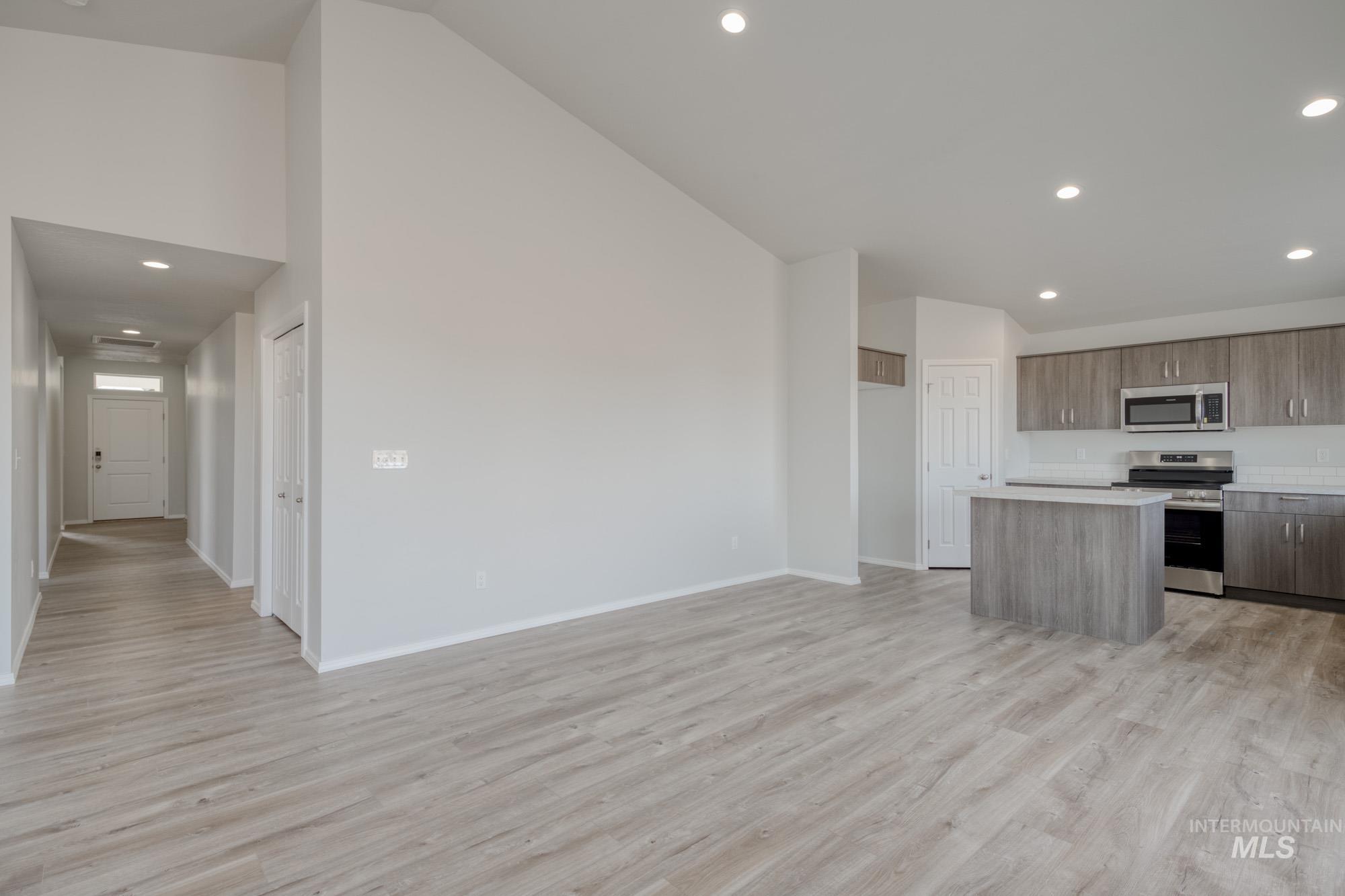 Kitchen featuring a kitchen island, recessed lighting, appliances with stainless steel finishes, light wood-type flooring, and high vaulted ceiling