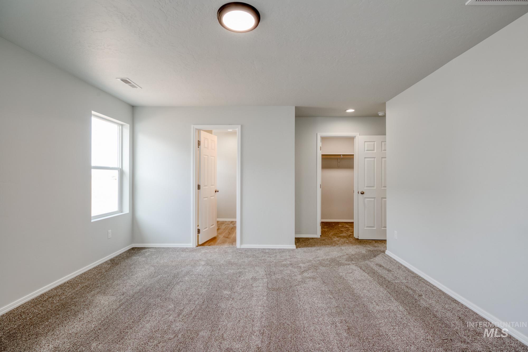 Unfurnished bedroom featuring a walk in closet, light carpet, and connected bathroom