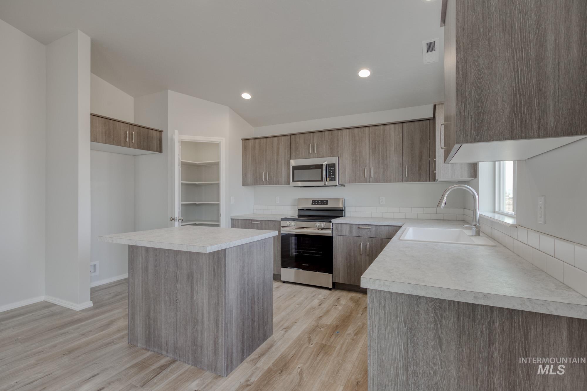 Kitchen featuring stainless steel appliances, a kitchen island, light countertops, light wood-type flooring, and recessed lighting